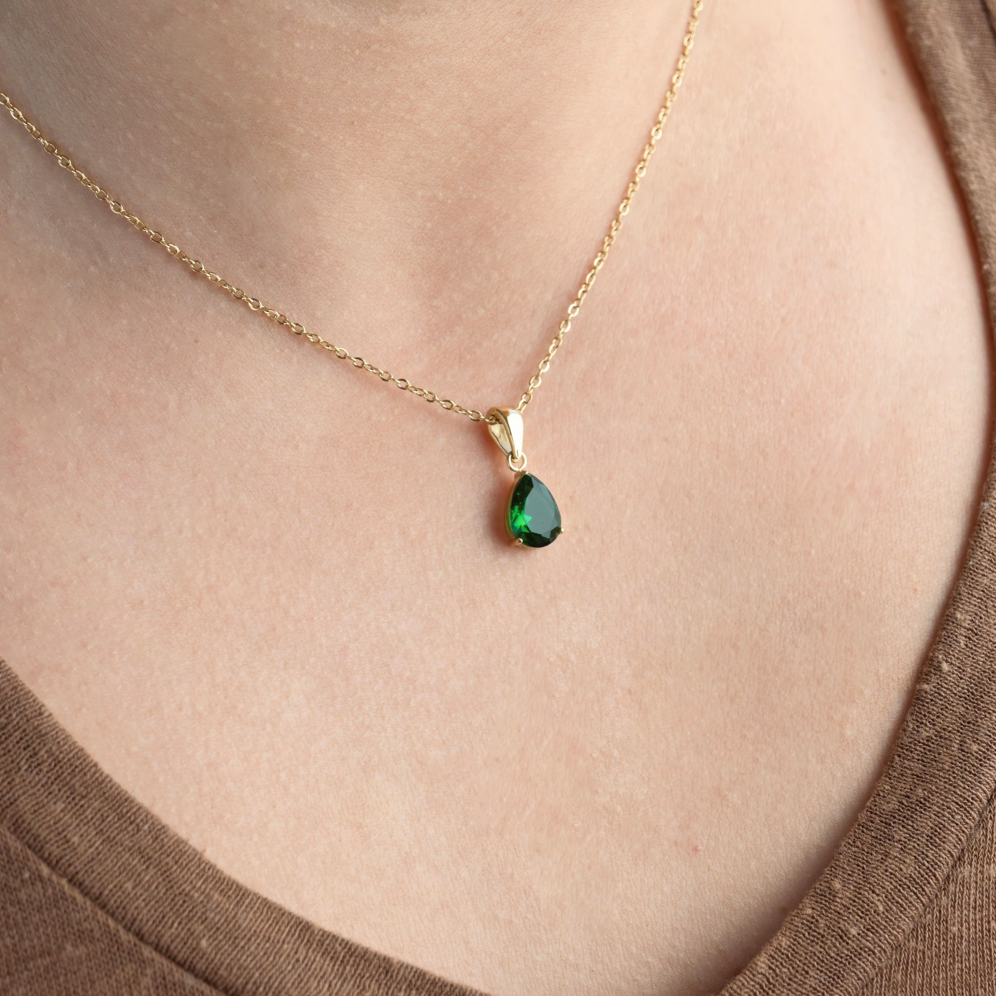 Gold may birthstone pendant on a person's neck.