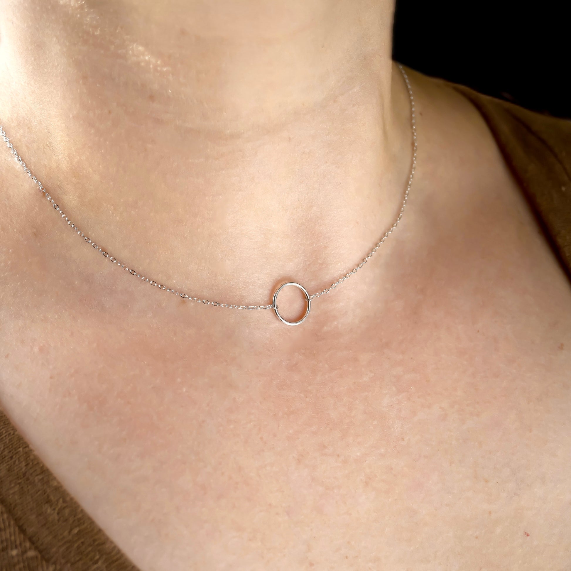 Silver necklace with a small ring pendant on a person's neck against a neutral background