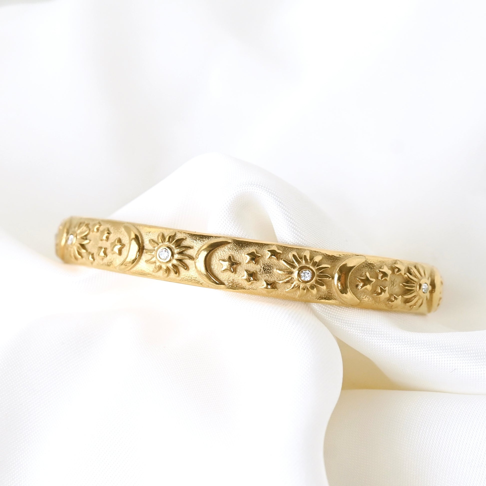 Gold open bangle with decorative sun, moon and stars on a white fabric background