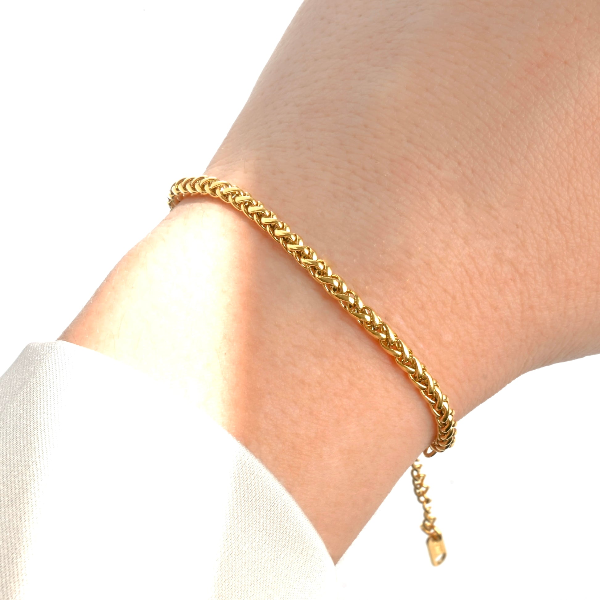 Gold wheat chain bracelet on a wrist with a white background under direct sunlight