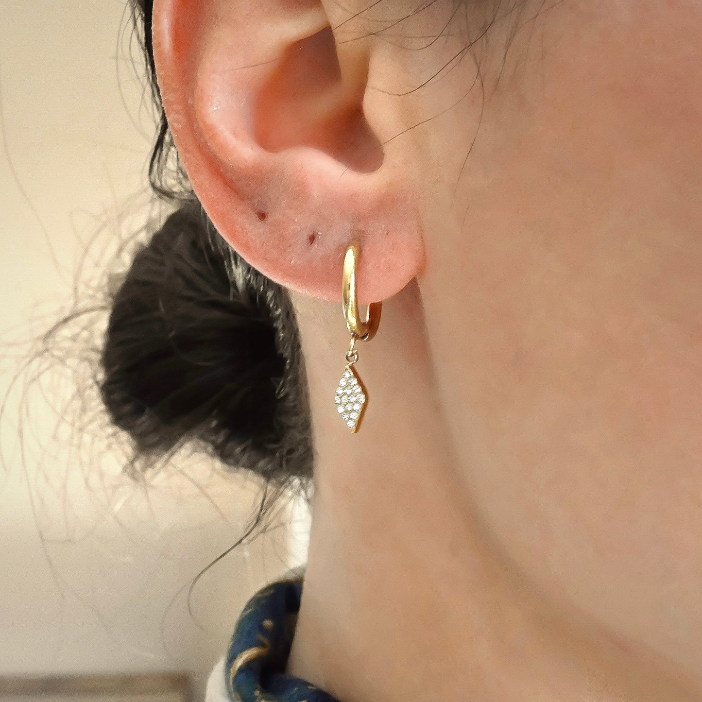 Gold huggie hoops with rhombus dangles pave set with clear stones on a person's ear