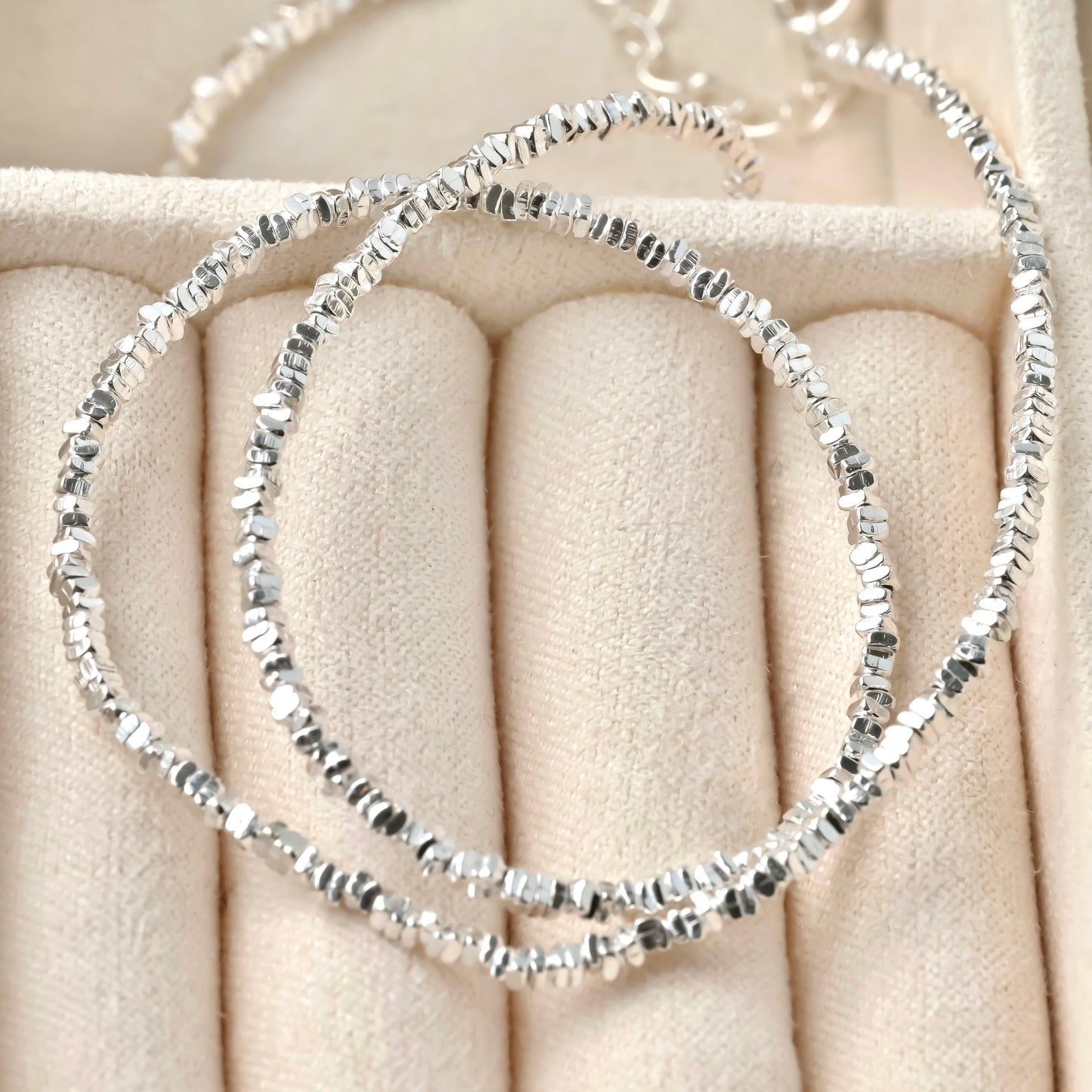 Silver beaded bracelet on a beige cushion