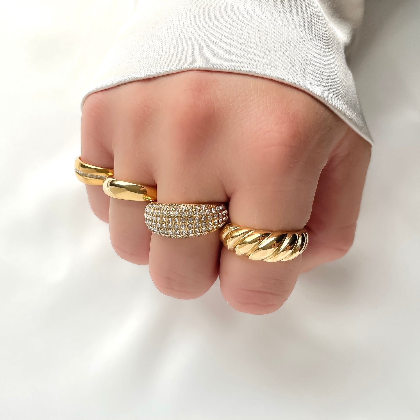 Hand wearing multiple chunky gold rings, the one on middle finger being the pave CZ dome ring, on a plain background