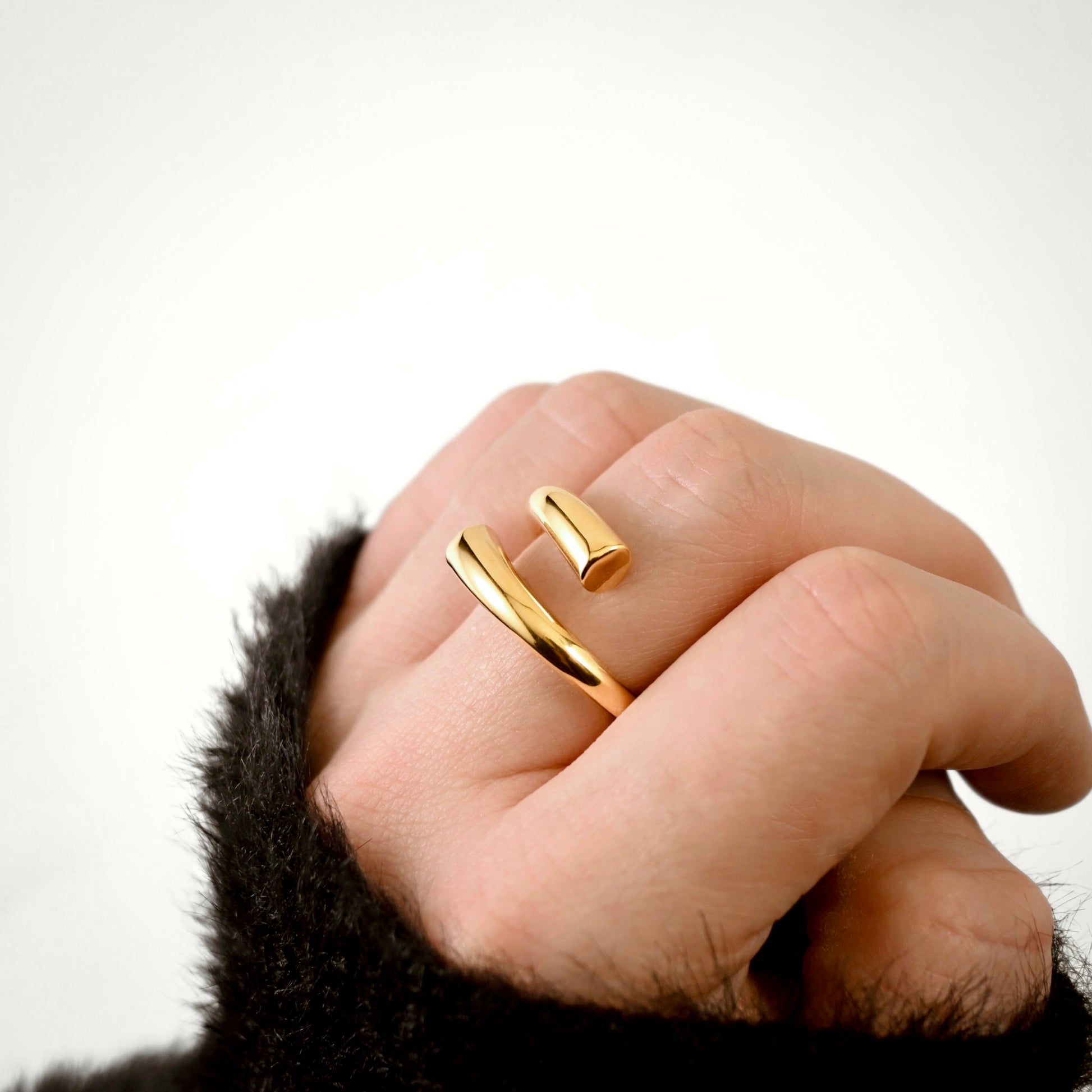 A close-up of a hand wearing a minimalist, open chunky gold cuff ring against a clean white background.