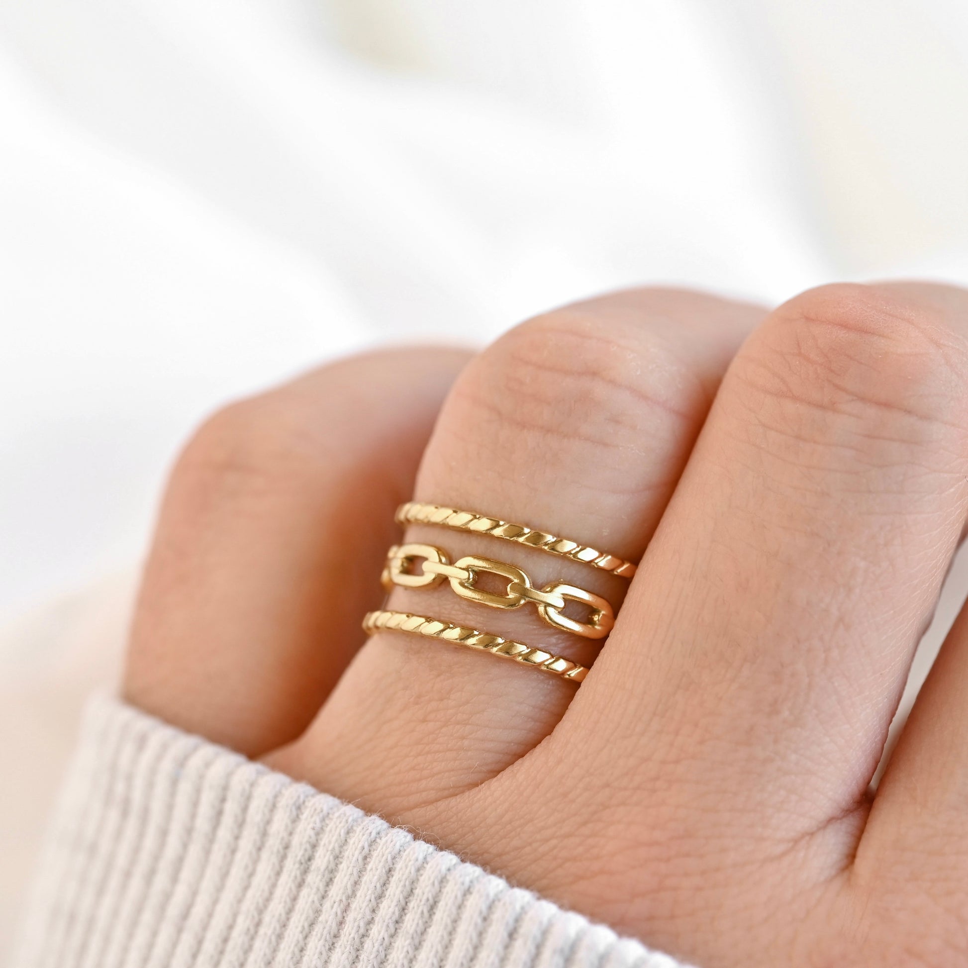Gold link ring on a finger against a white background