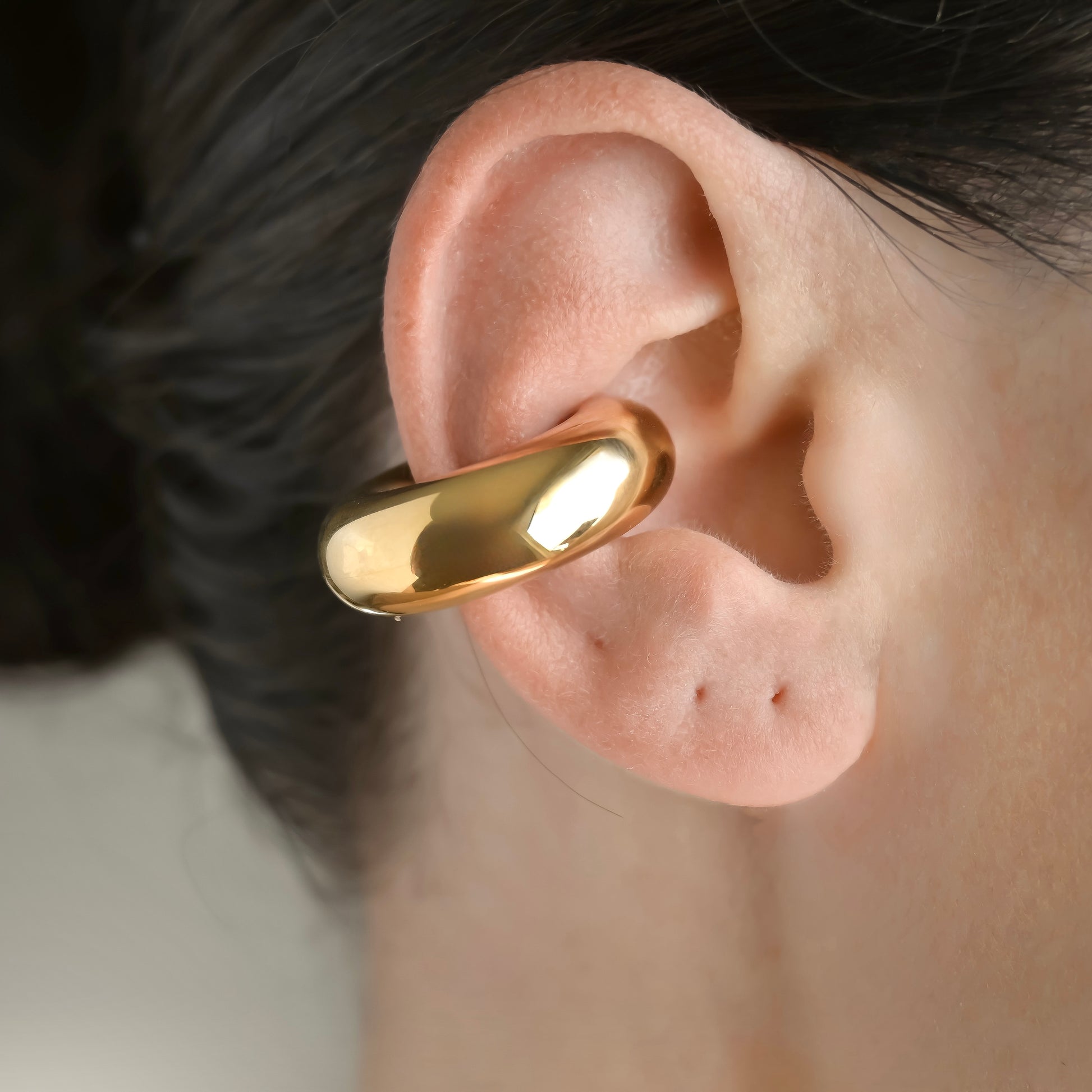 Large gold earcuff worn on a person's ear with a neutral background