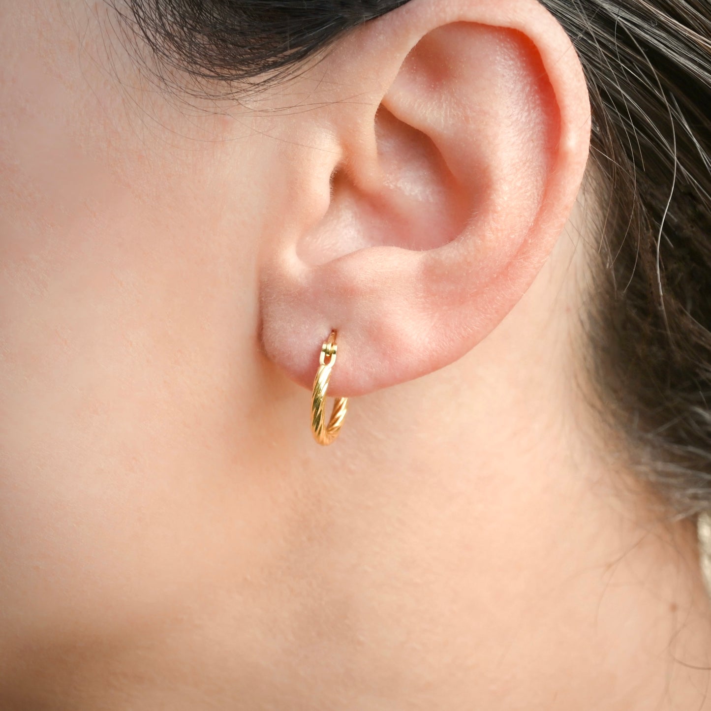 Side view of Gold twist hoop earring worn by a person