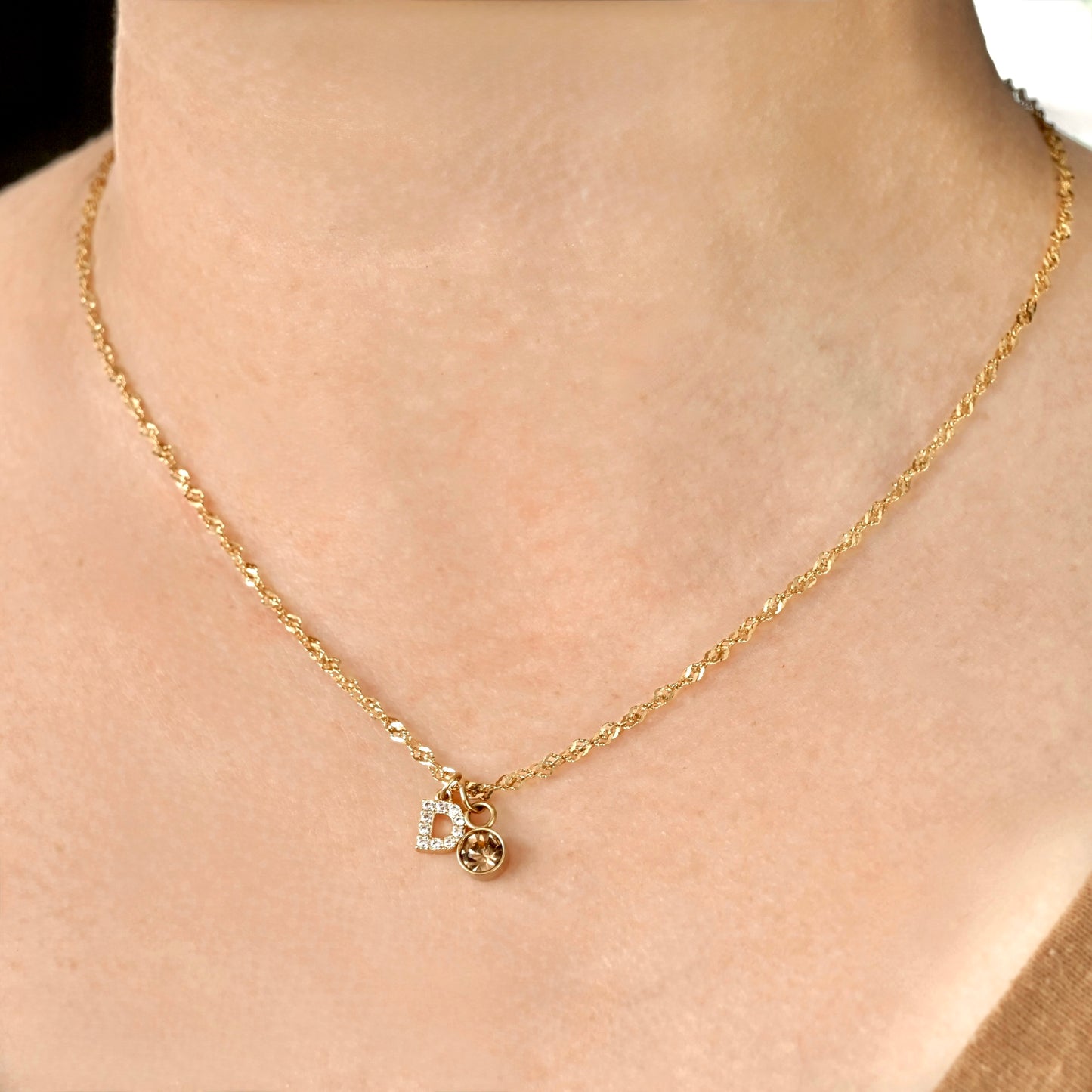 Gold twisted chain with a diamond 'D' pendant  and november birthstone on a person's neck against a neutral background