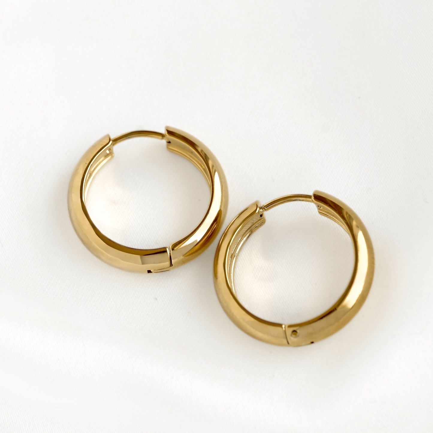 A pair of polished 21 mm gold huggie hoop earrings on a clean white background.