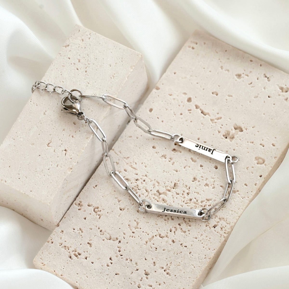 Silver paperclip necklace with engraved names on a textured beige surface