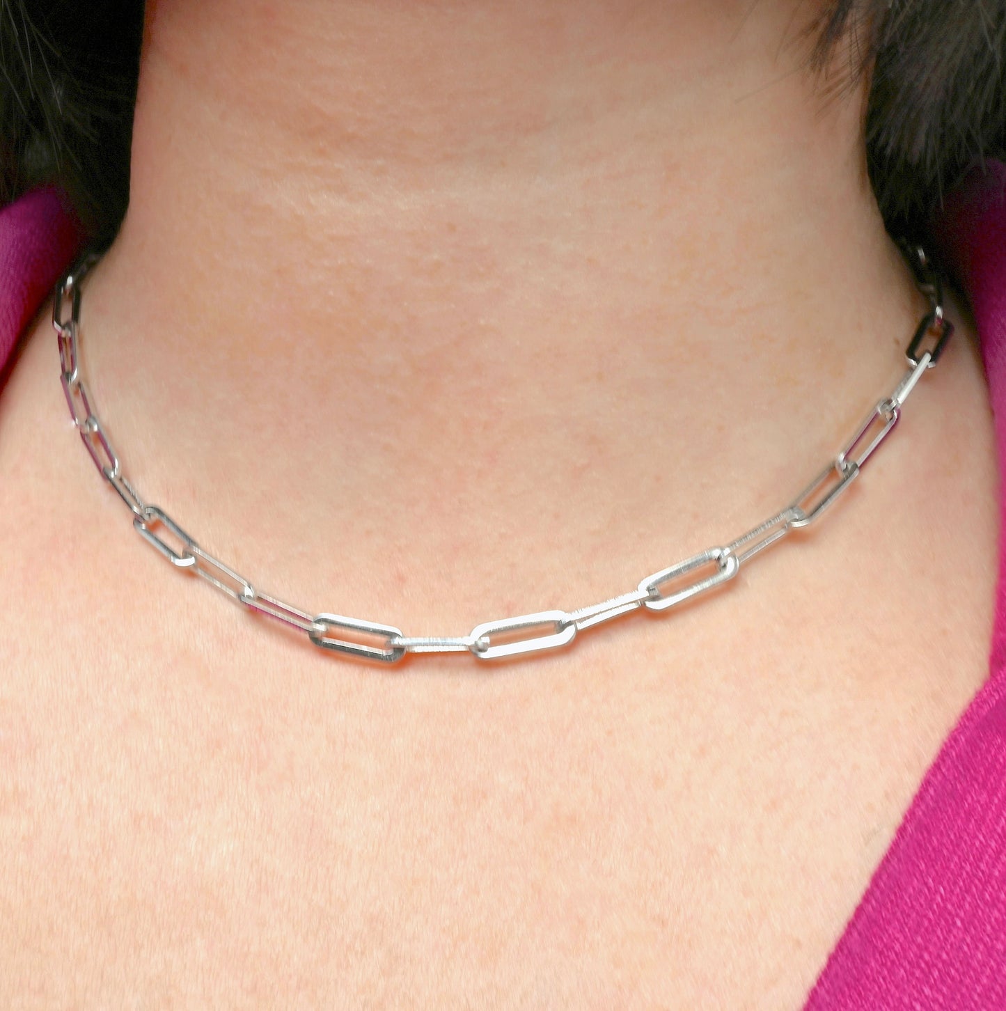 Front view of chunky silver paperclip chain necklace worn by a person with a pink top