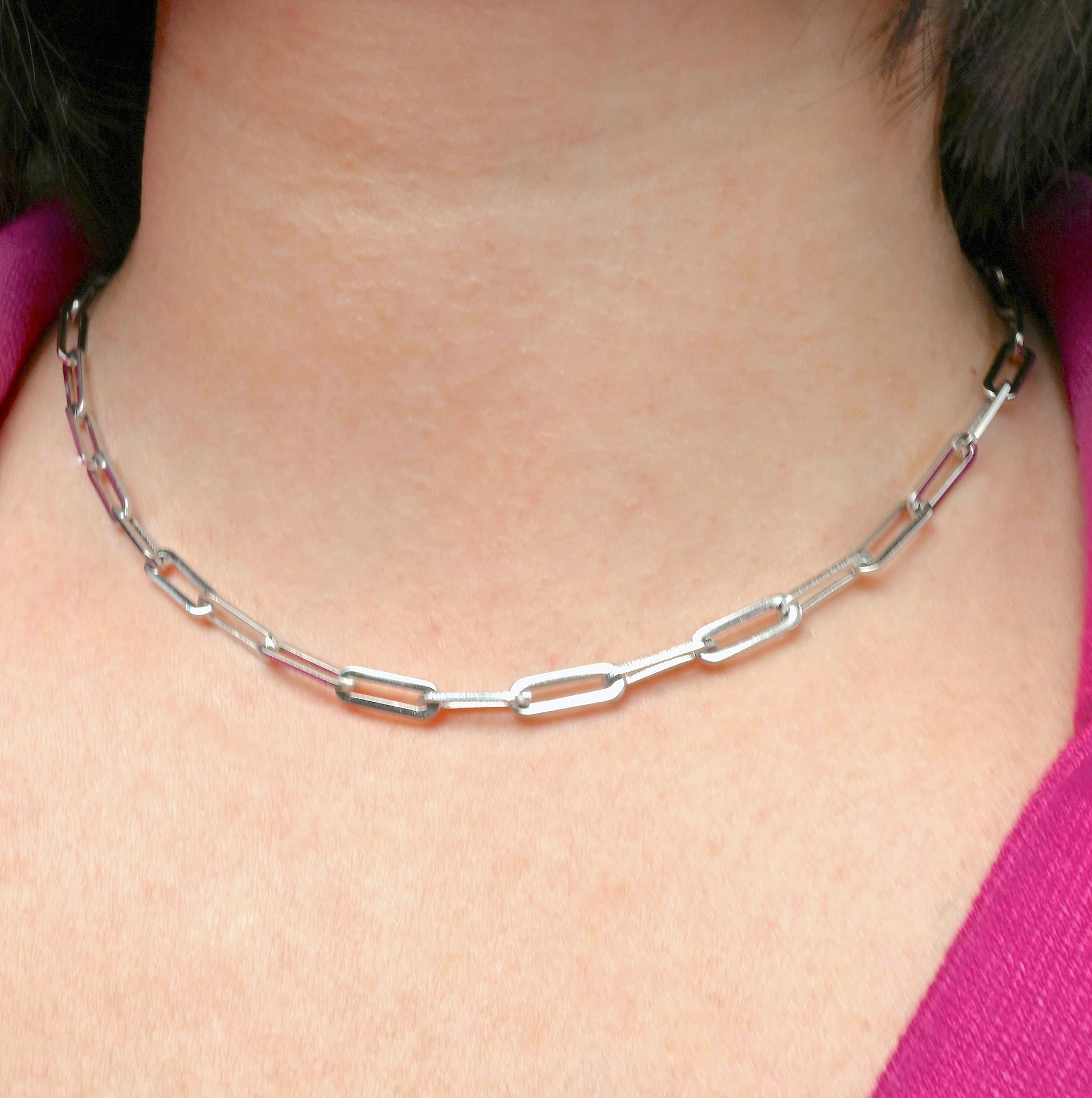Front view of chunky silver paperclip chain necklace worn by a person with a pink top