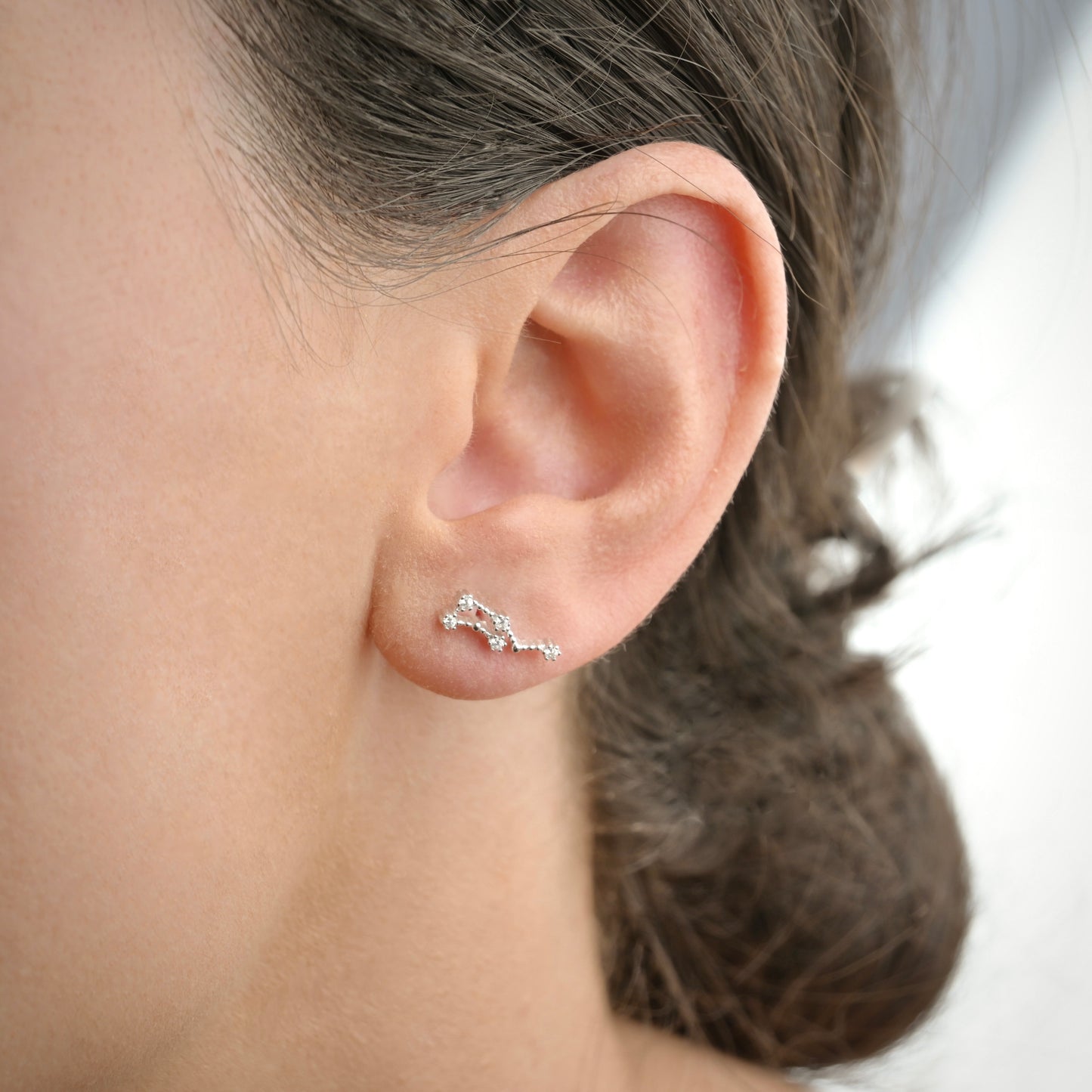Close-up of an ear wearing a delicate zodiac earrings with a blurred background
