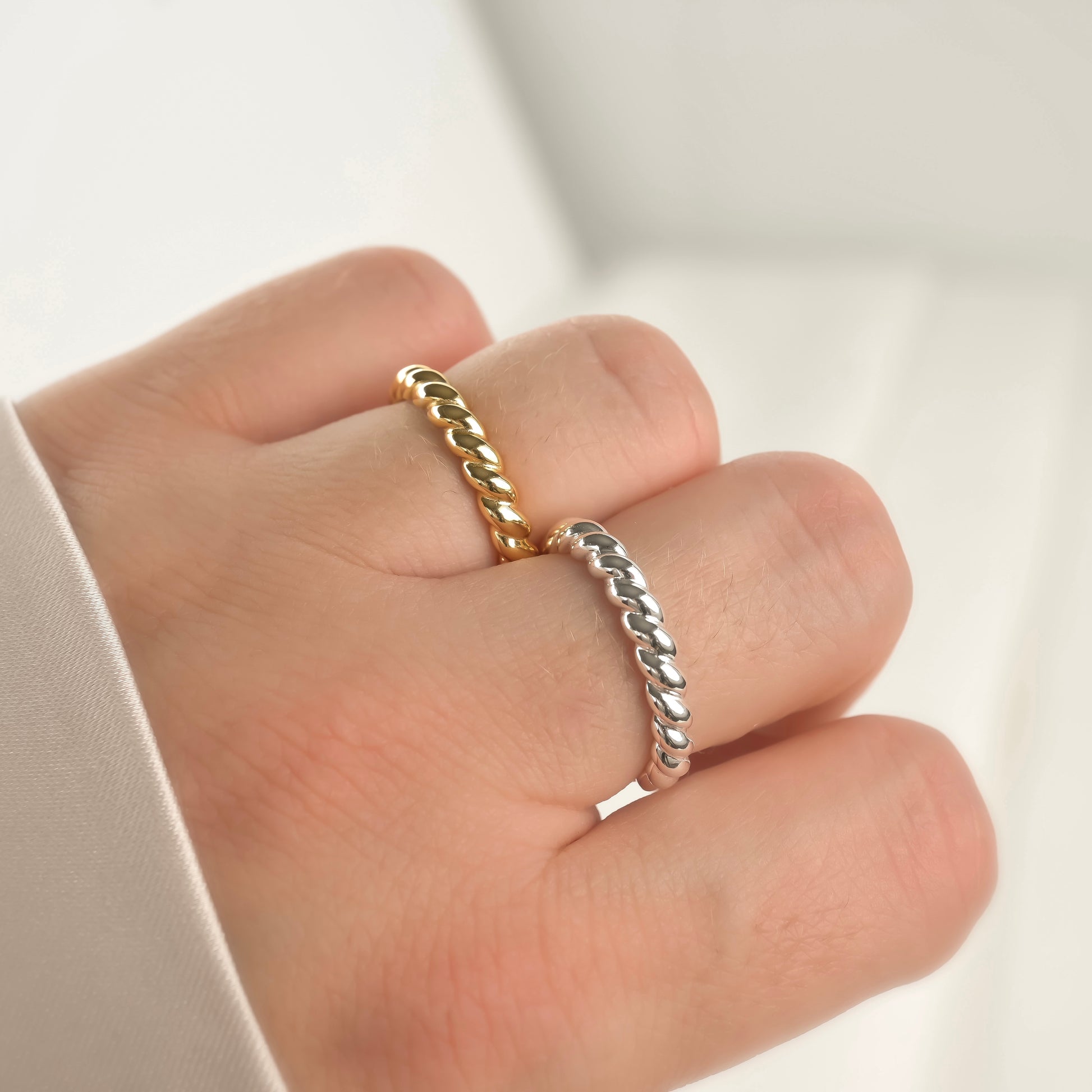 Gold and silver twisted rings on a hand against a neutral background