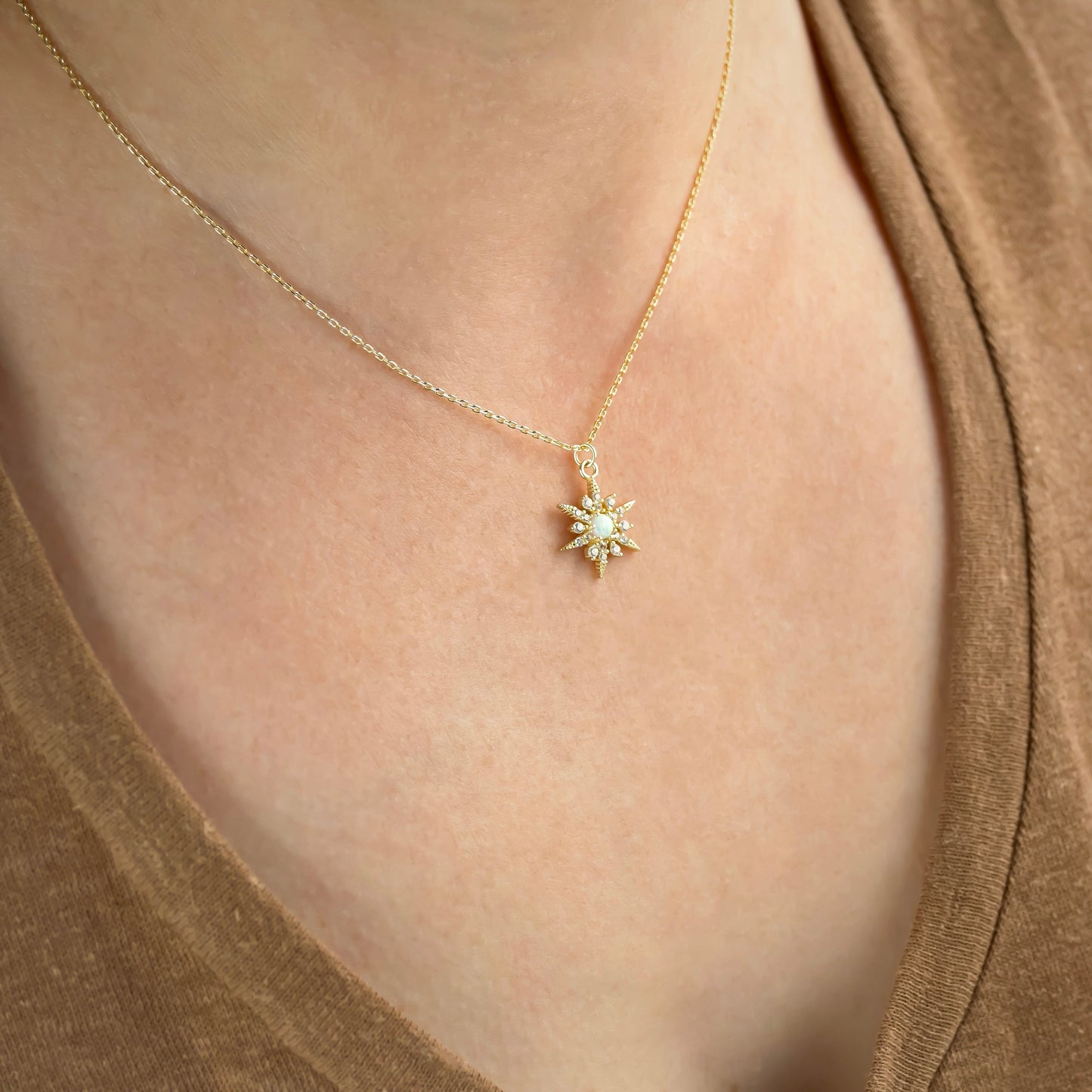 Gold necklace with a opal star-shaped pendant on a person wearing a brown top.