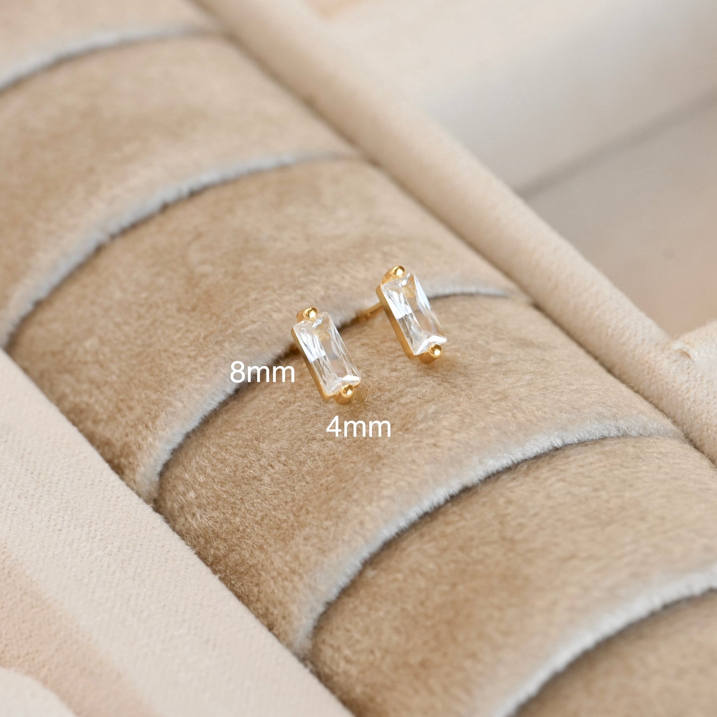 Gold CZ stud earrings on a textured beige surface with size labels.