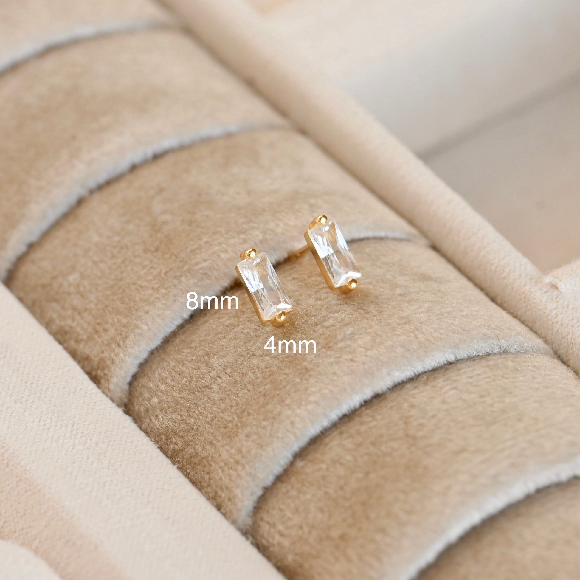 Gold CZ stud earrings on a textured beige surface with size labels.