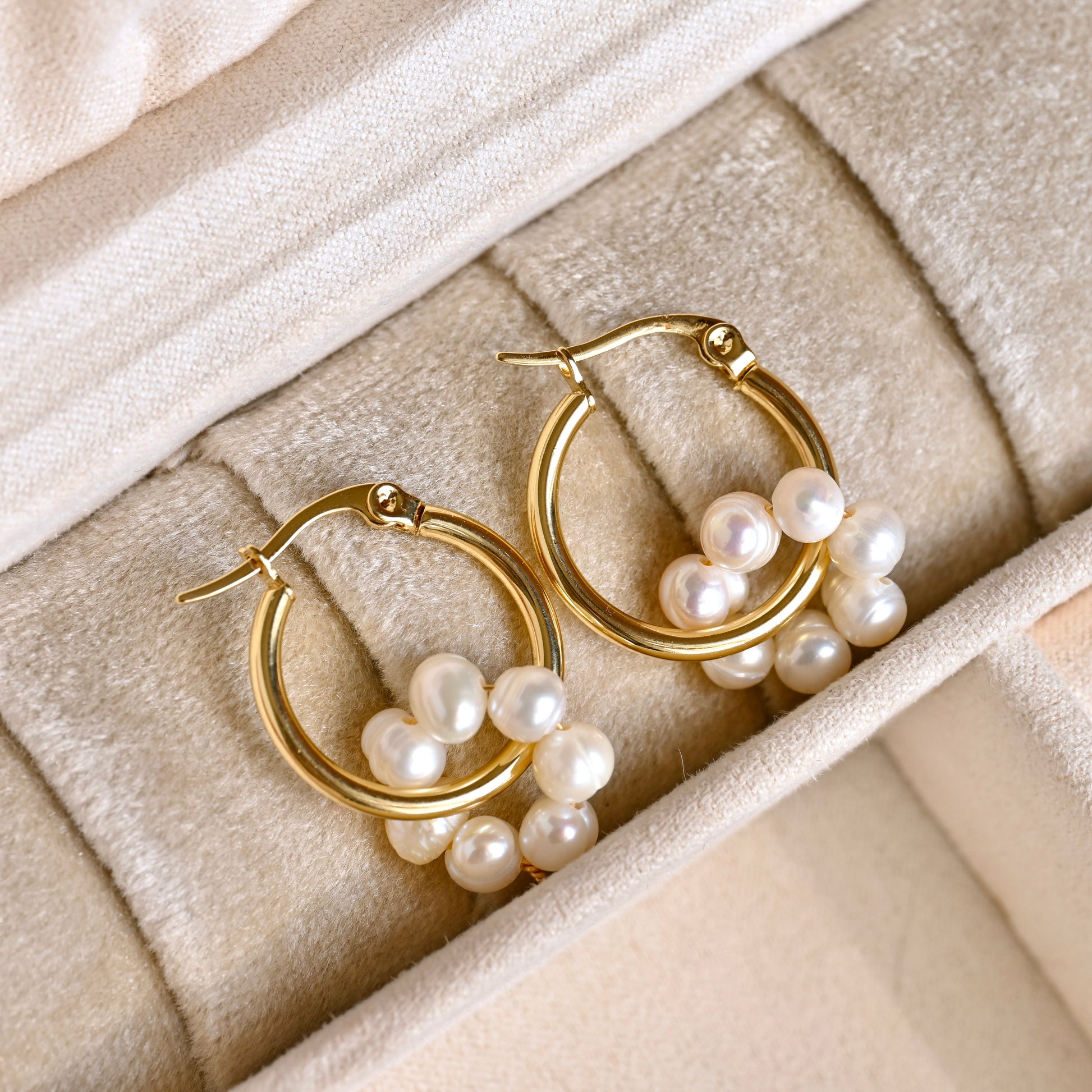 Gold hoop earrings with genuine pearl accents on a beige fabric background