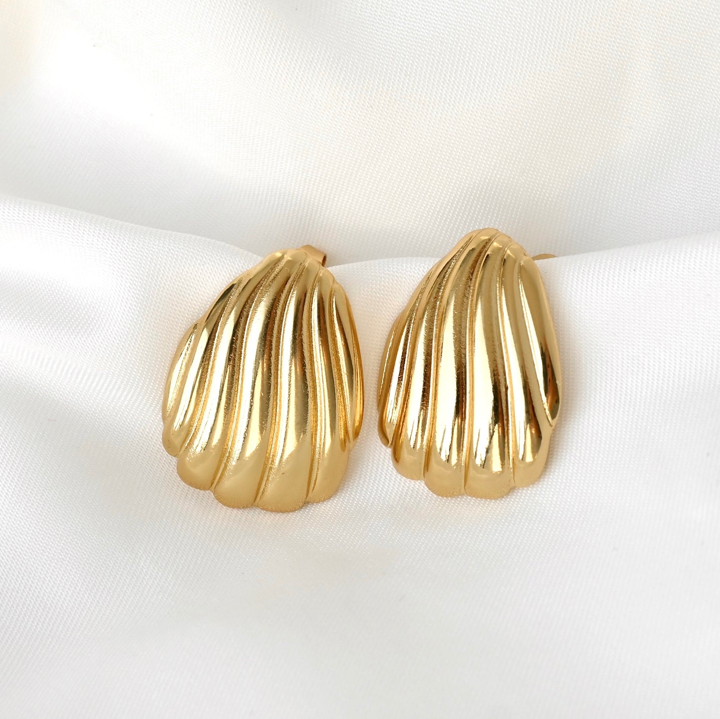 Gold shell-shaped earrings on a white satin surface