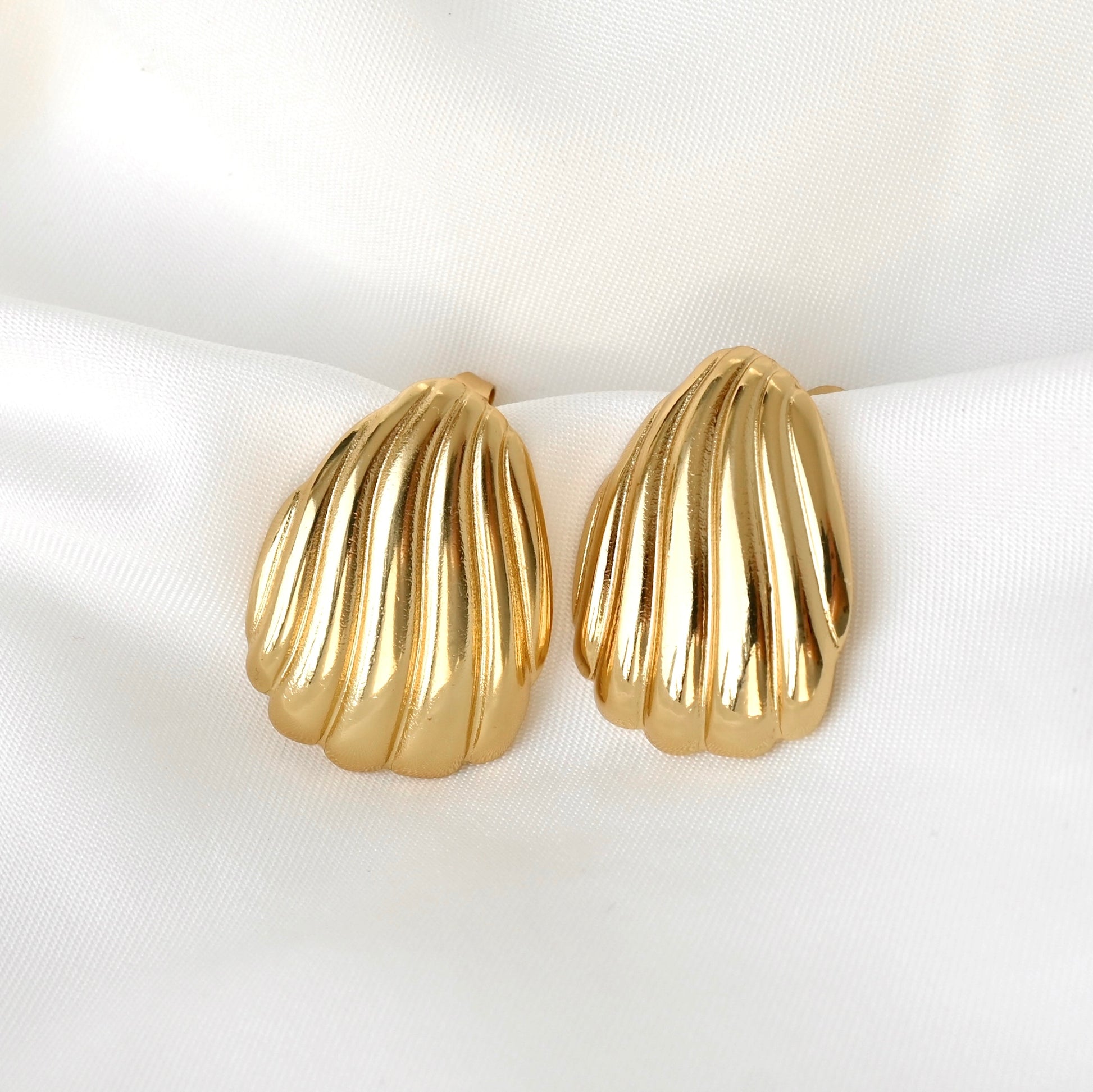 Gold shell-shaped earrings on a white satin surface