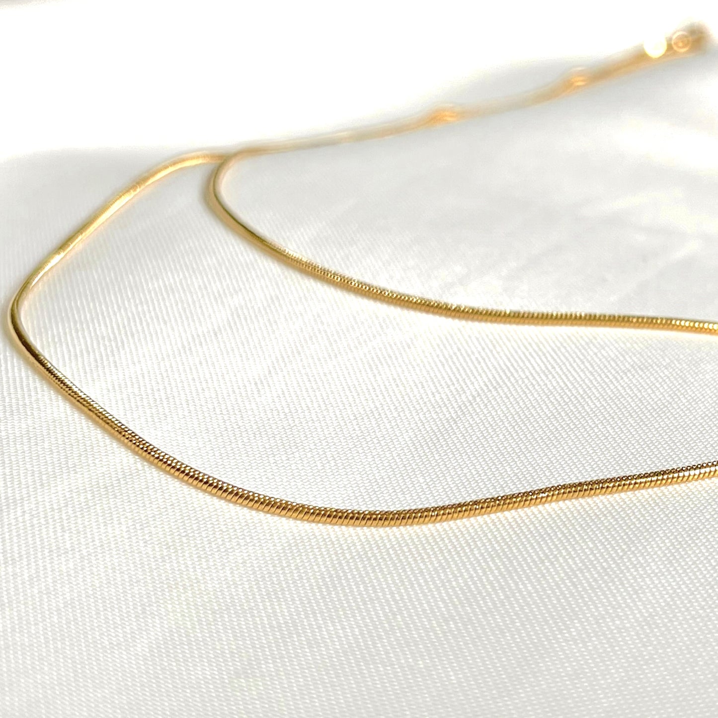 Layered gold necklace on a white fabric background