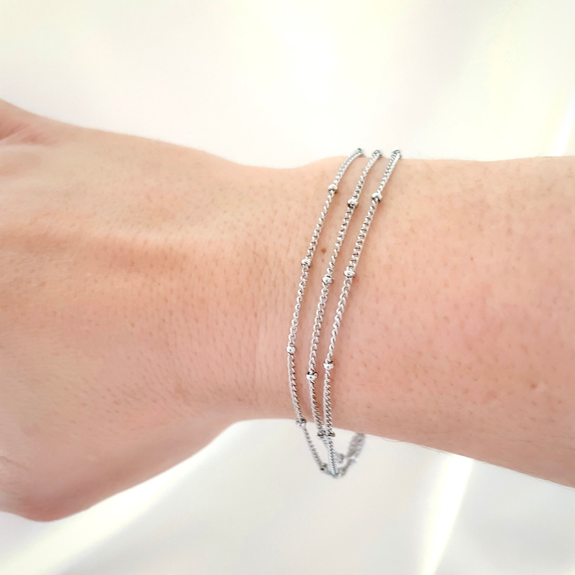 Three-layered stainless steel bracelet on a wrist against a white background