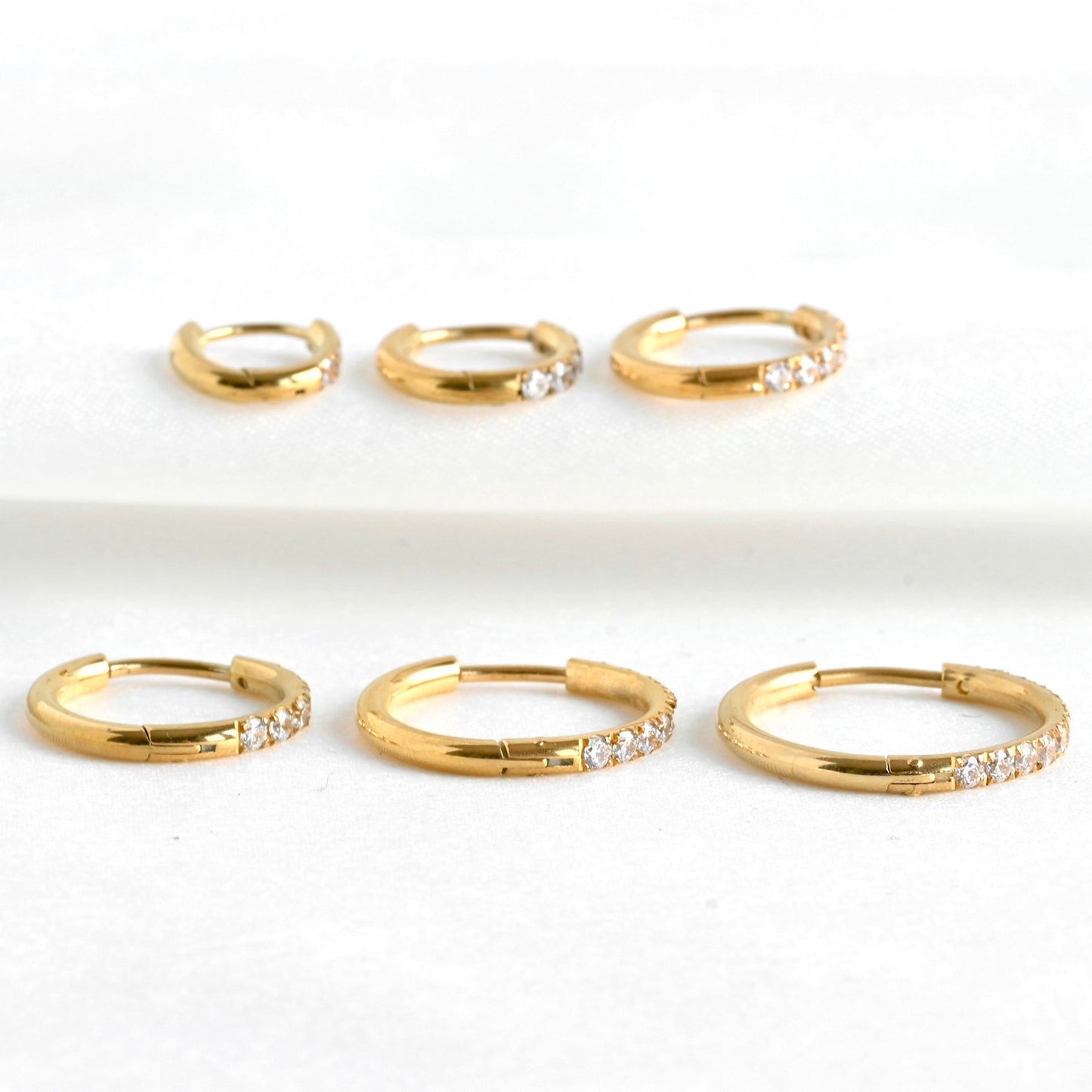 Set of gold half cz half plain hoops with small simulated diamonds on a white background