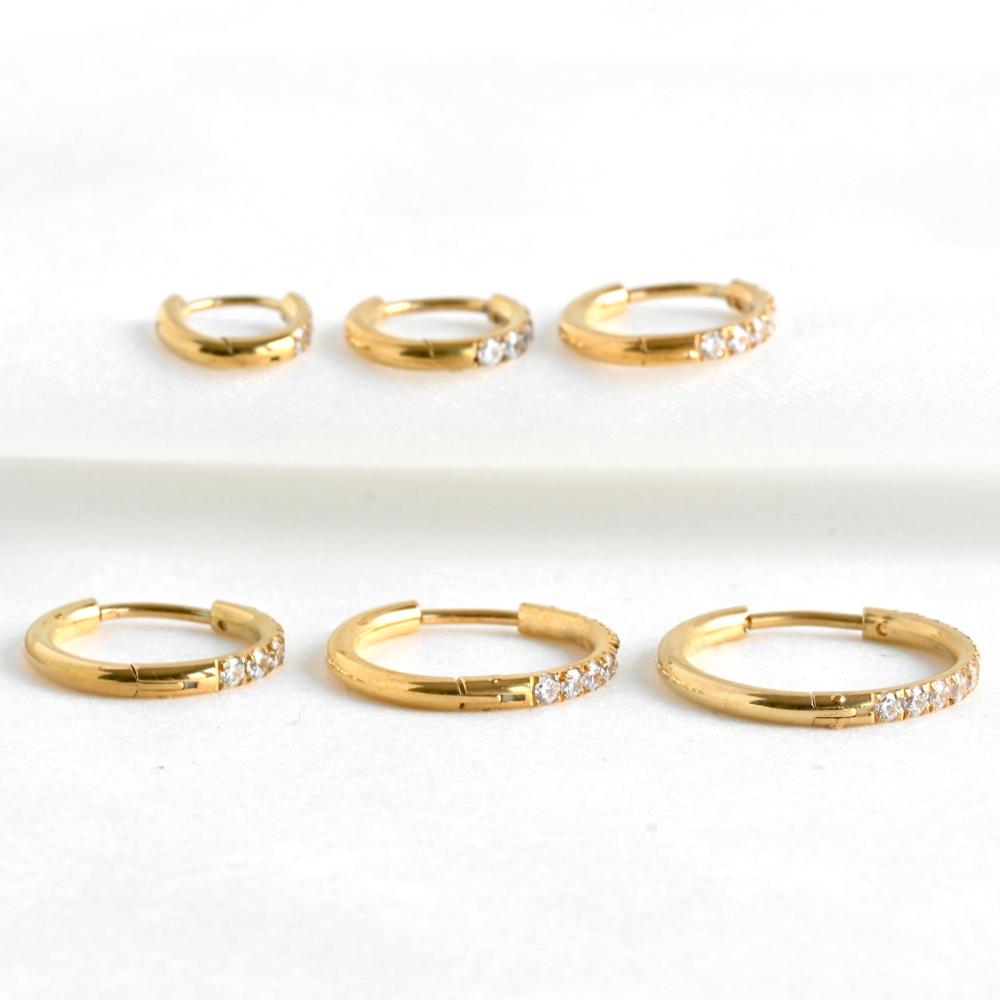 Set of gold half cz half plain hoops with small simulated diamonds on a white background