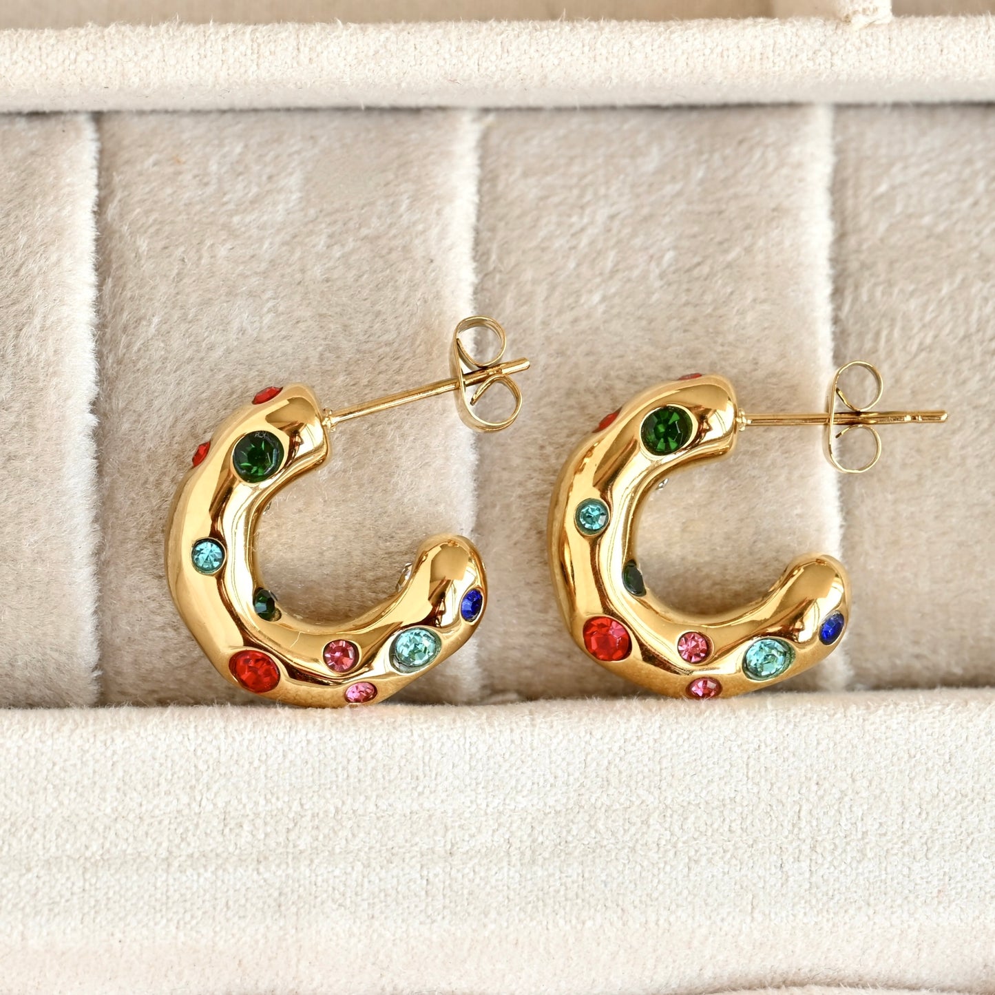 Gold organic shaped thick hoop earrings with multicolor CZ stones and posts in a beige jewelry box