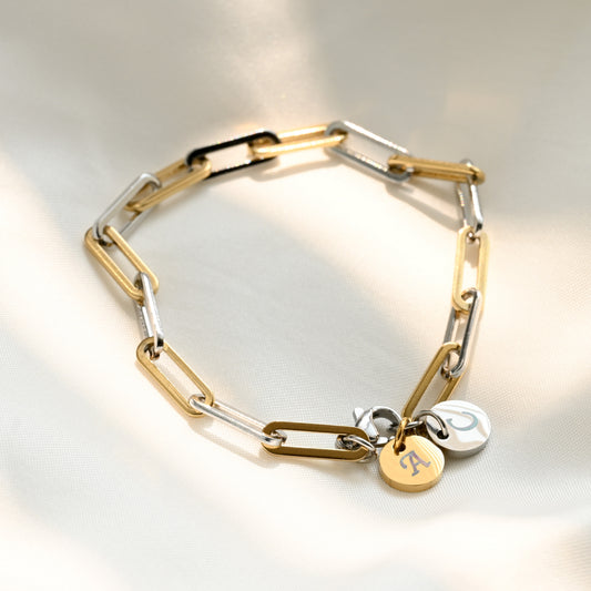 two-toen bracelet with one gold and one silver round initial charm on a light gray background