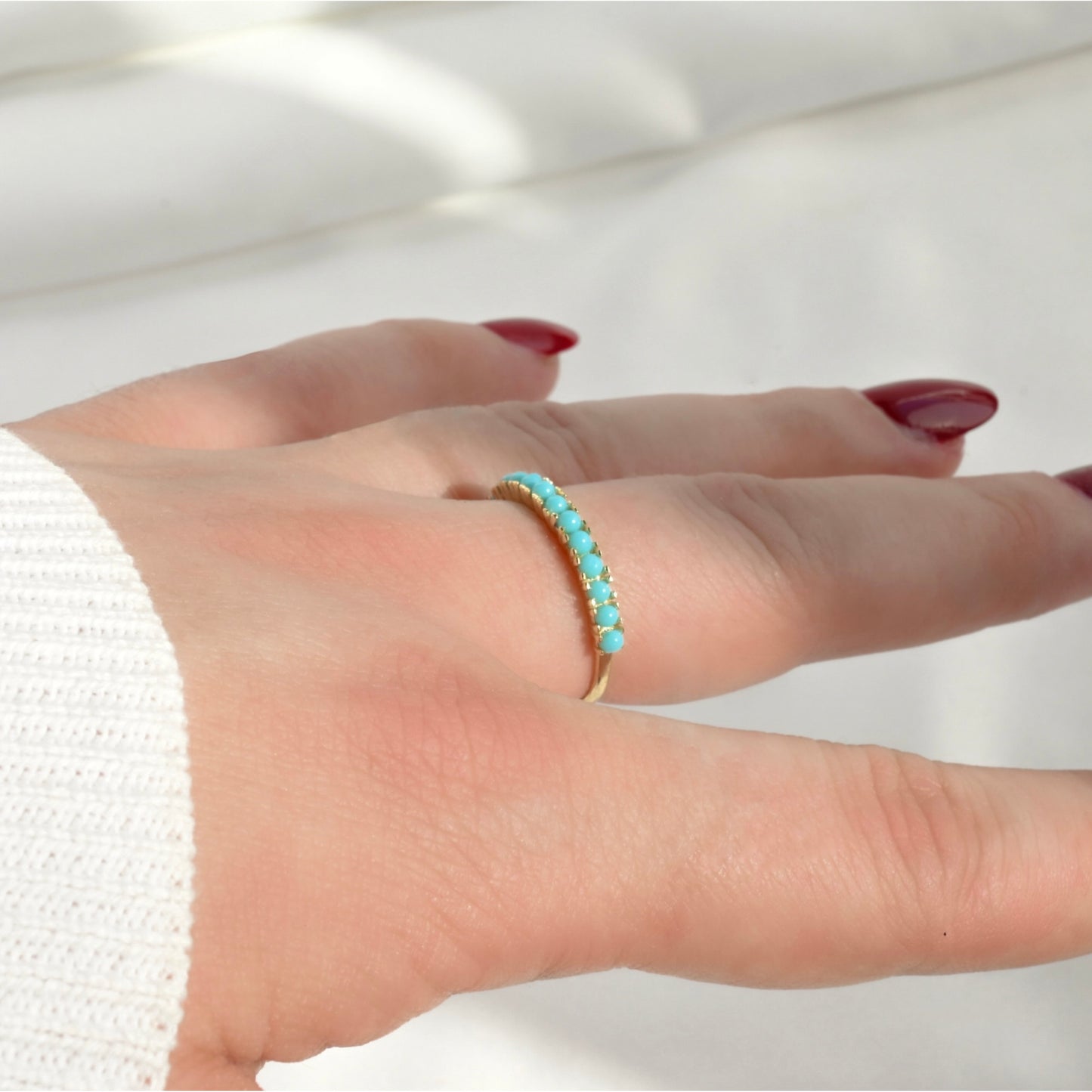 Hand wearing a turquoise ring on a plain background, the turquoise stones look light and warm under direct sunlight.