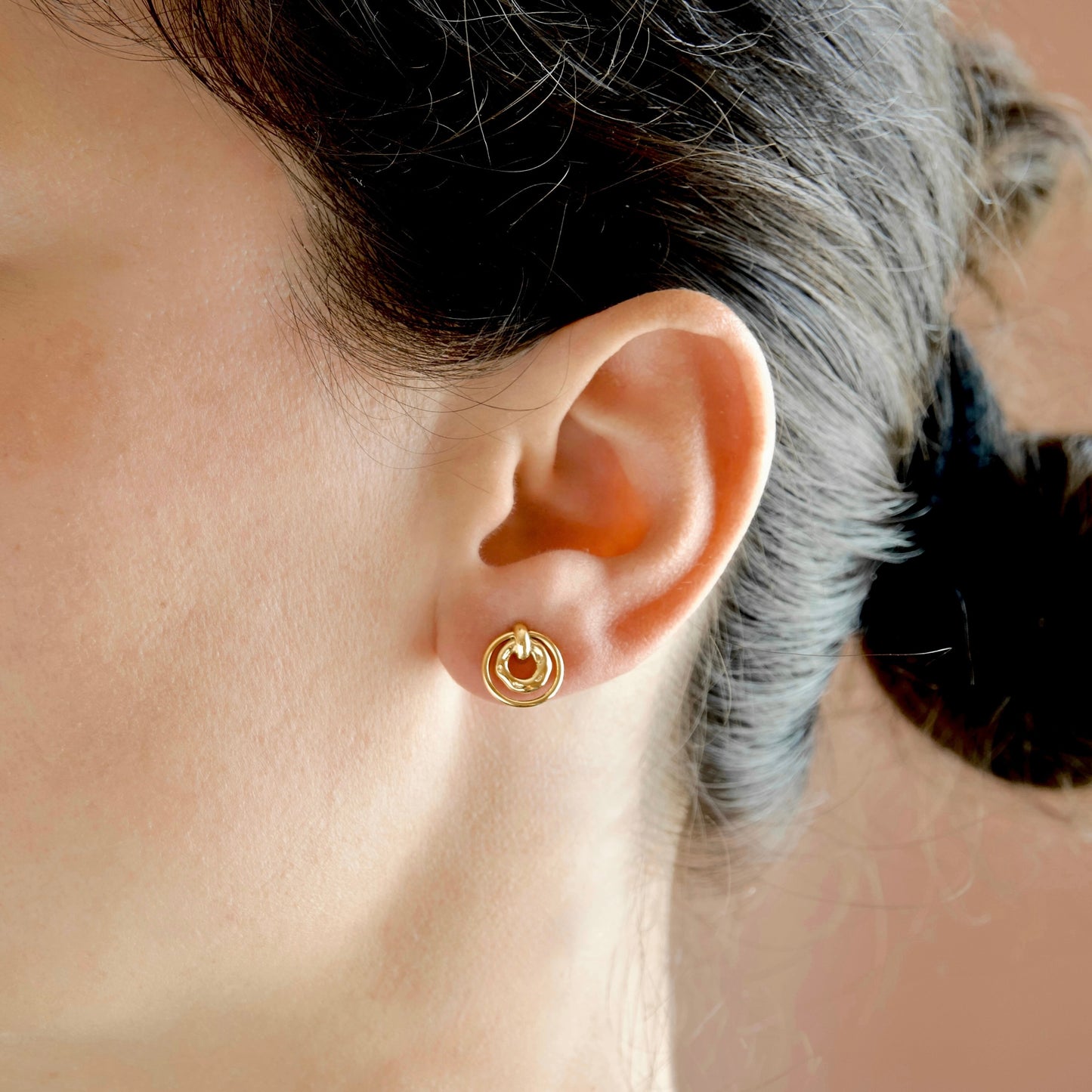 A close-up of a person's ear wearing a small gold hoop earring with a circular inner detail.
