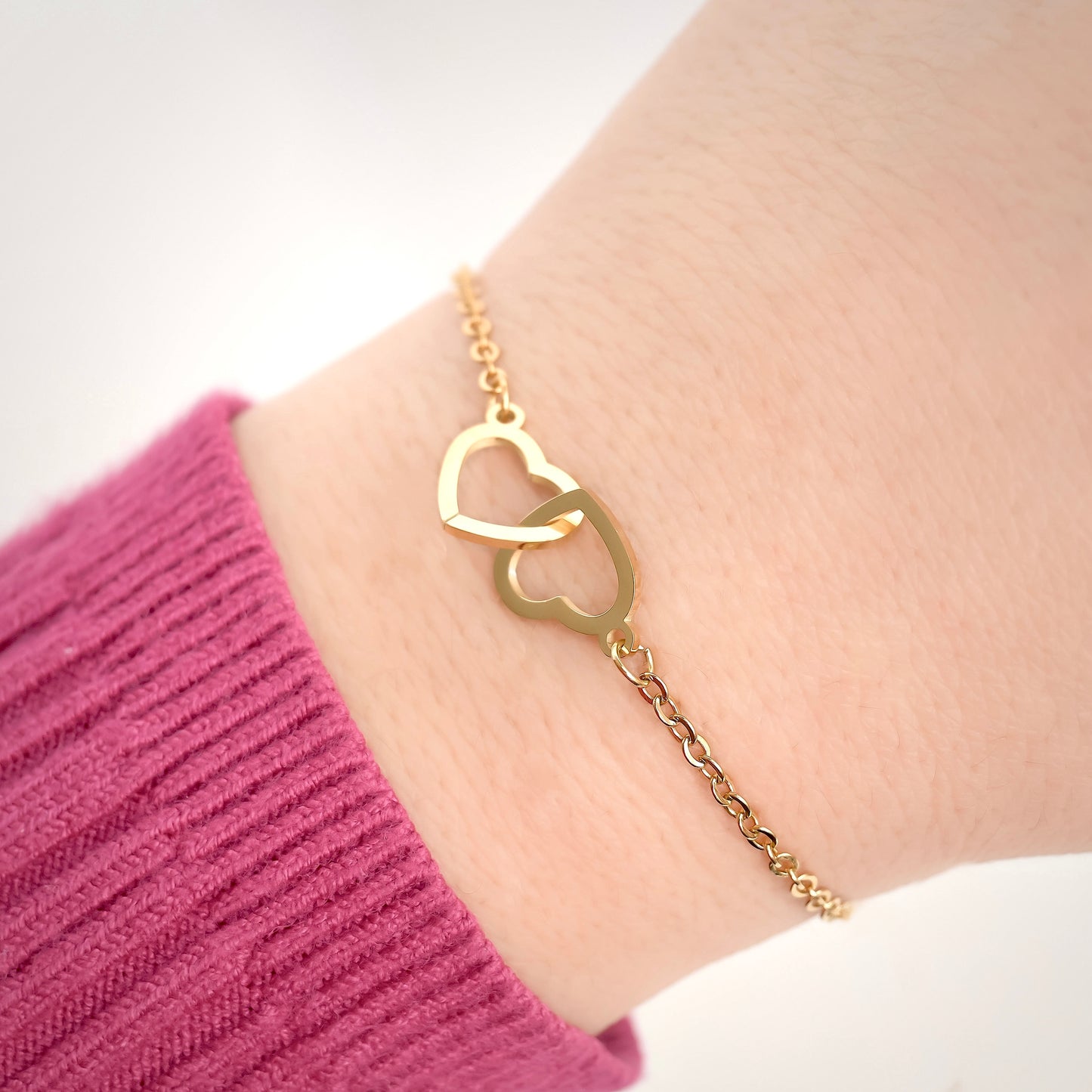 Gold bracelet with interlocking hearts on a wrist against a white background