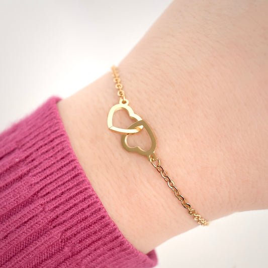 Gold bracelet with interlocking hearts on a wrist against a white background