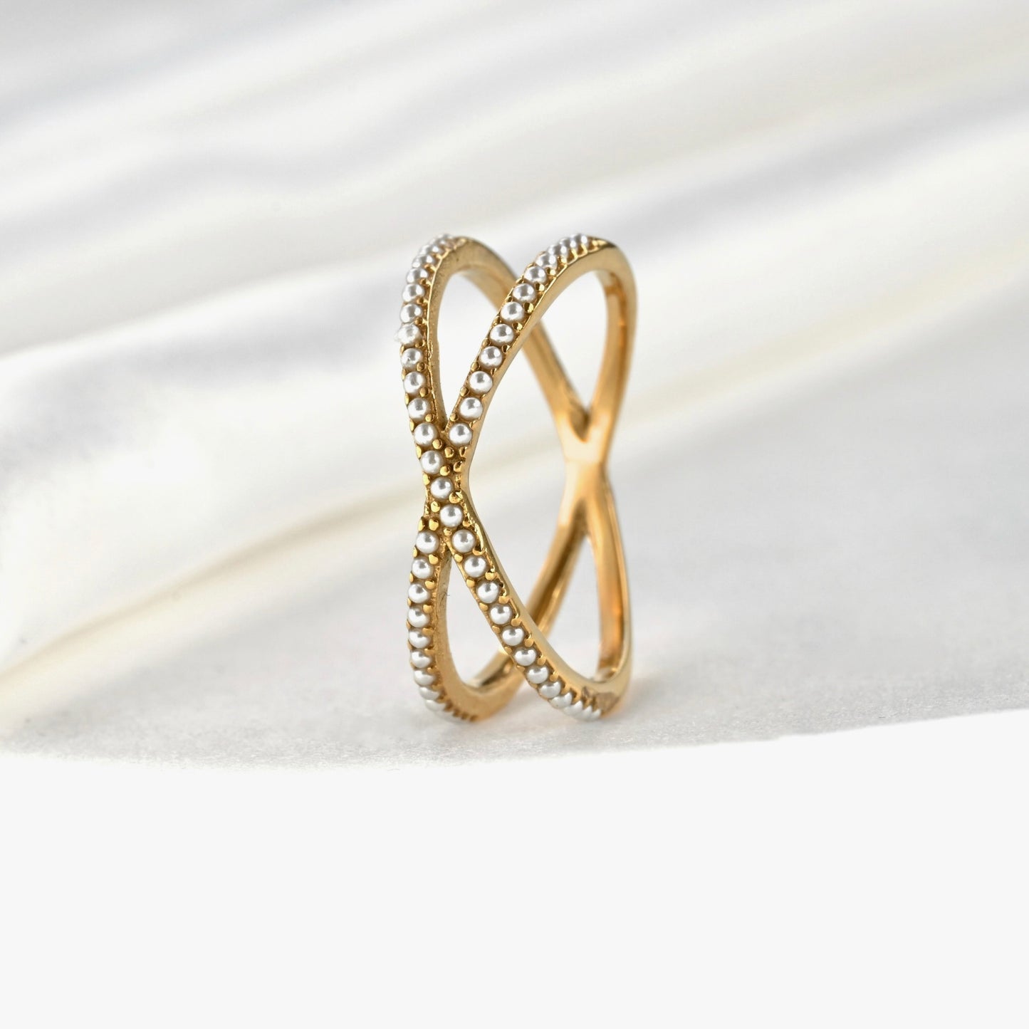 Gold pearl ring with beaded design standing vertically on a white satin background