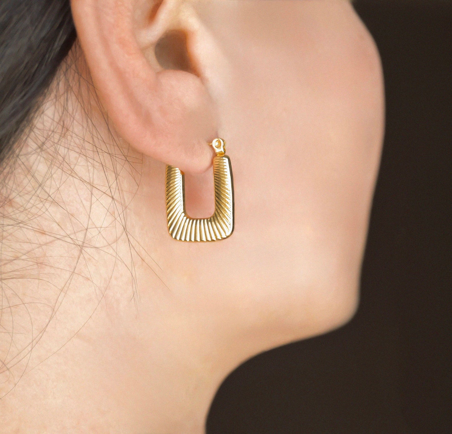 Gold hoop earring worn on an ear with a dark background