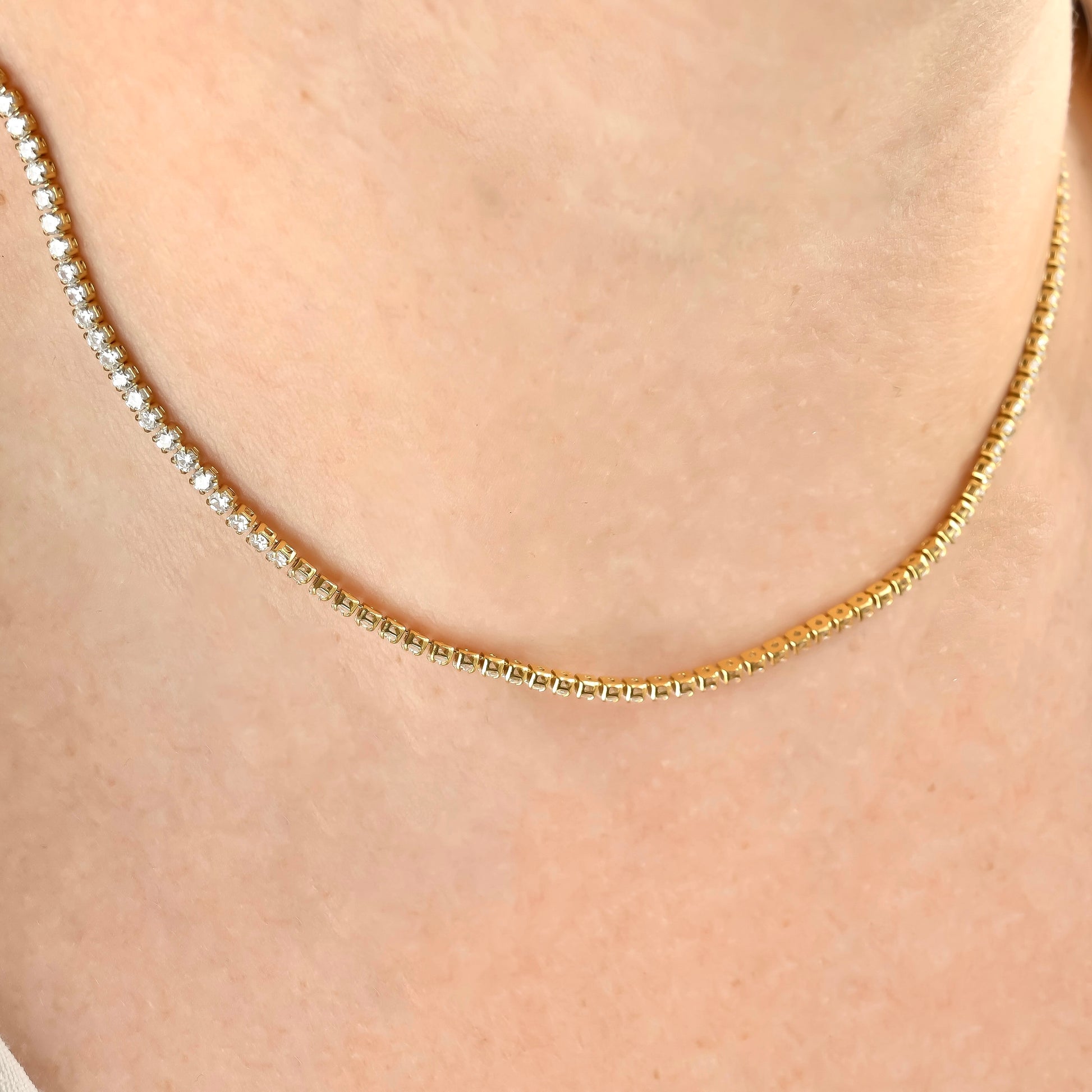 Gold stone and cup chain necklace on a person's neck against a neutral background