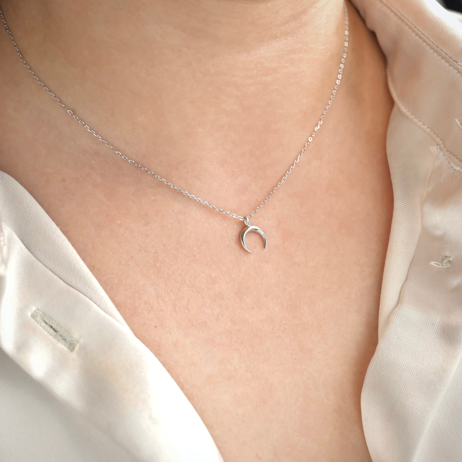 Silver necklace with a moon pendant on a person wearing a white blouse.