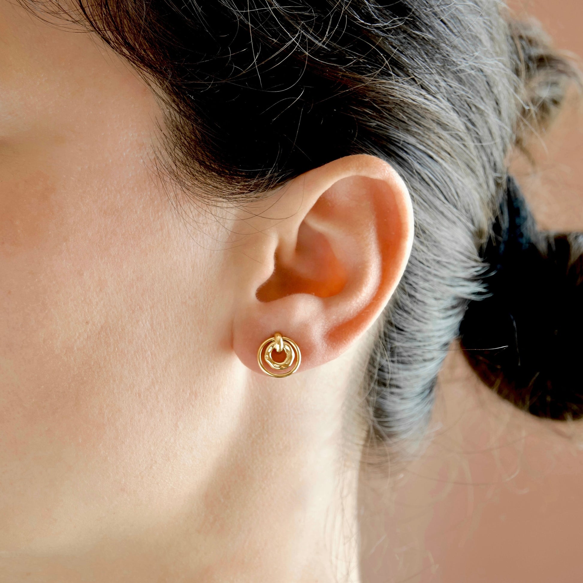 A close-up of a person's ear wearing a small gold hoop earring with a circular inner detail.