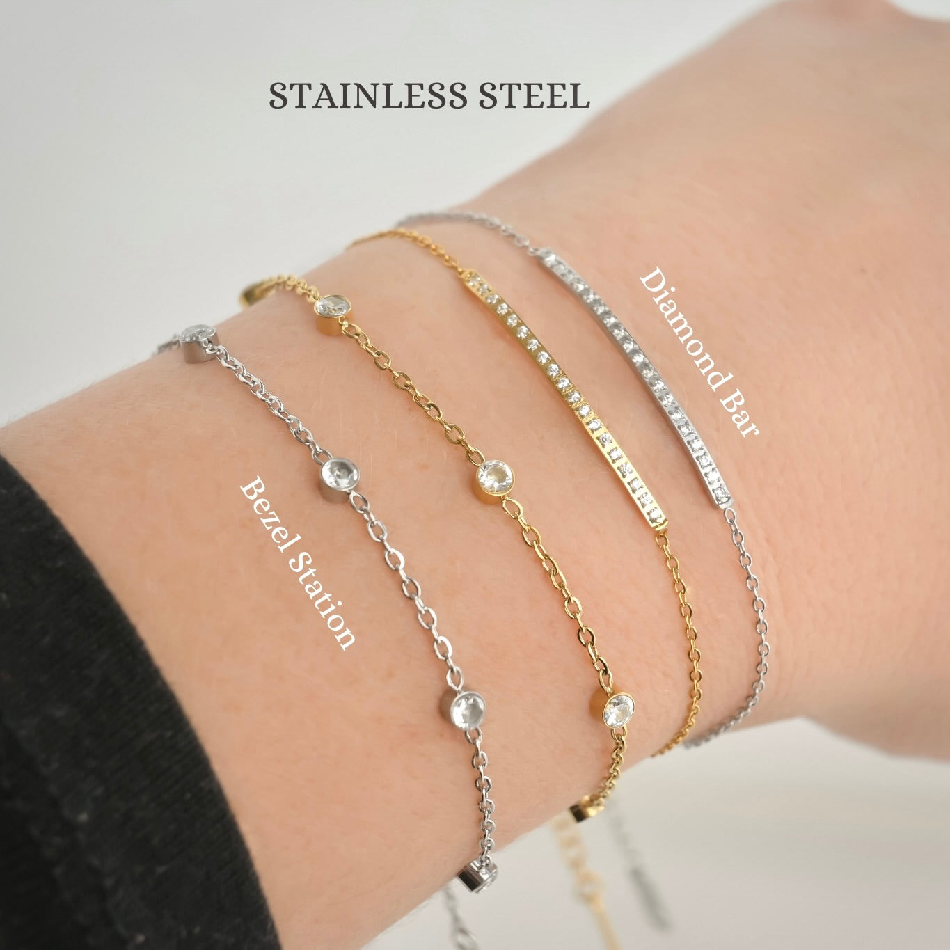 Wrist wearing four stainless steel bracelets, 2 diamond bars, and two bezel stations in gold and silver,  with 'STAINLESS STEEL' label on top 