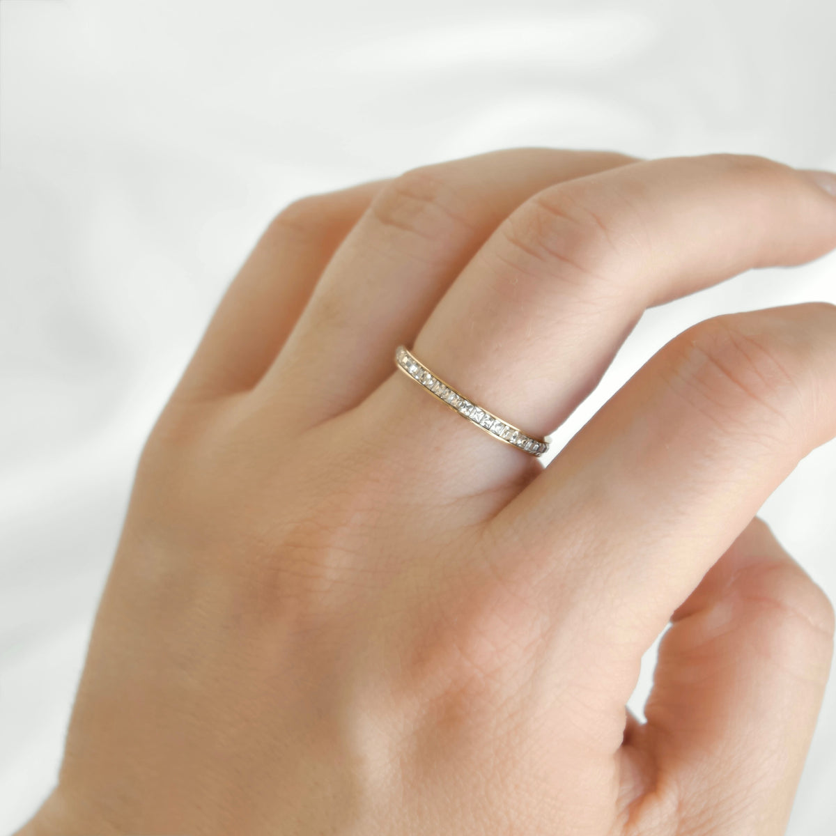 Slim gold eternity ring with channel set squre cubic zirconia stones on a woman's middle finger.
