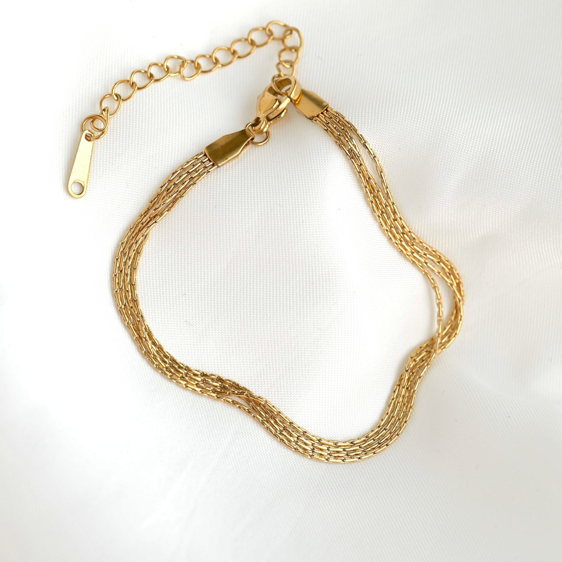 A gold-toned multi-strand chain bracelet with a lobster clasp and extension chain, displayed on a white textured fabric background.