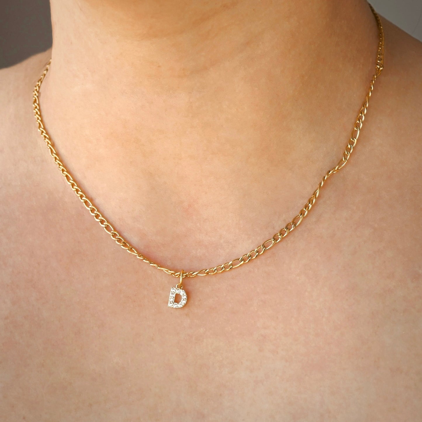Gold chain necklace with a diamond 'D' pendant on a person's neck.