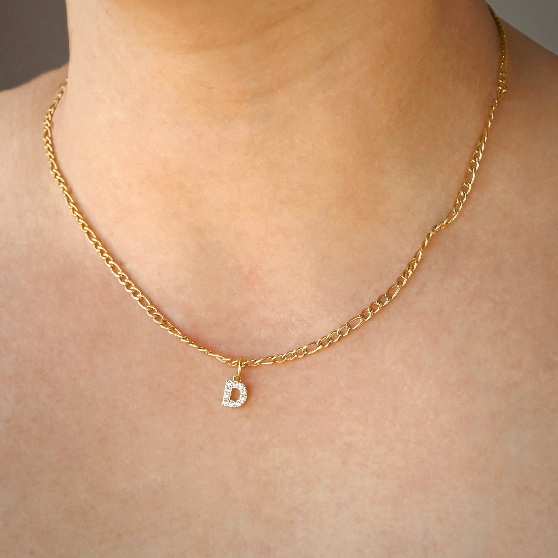 Gold chain necklace with a diamond 'D' pendant on a person's neck.