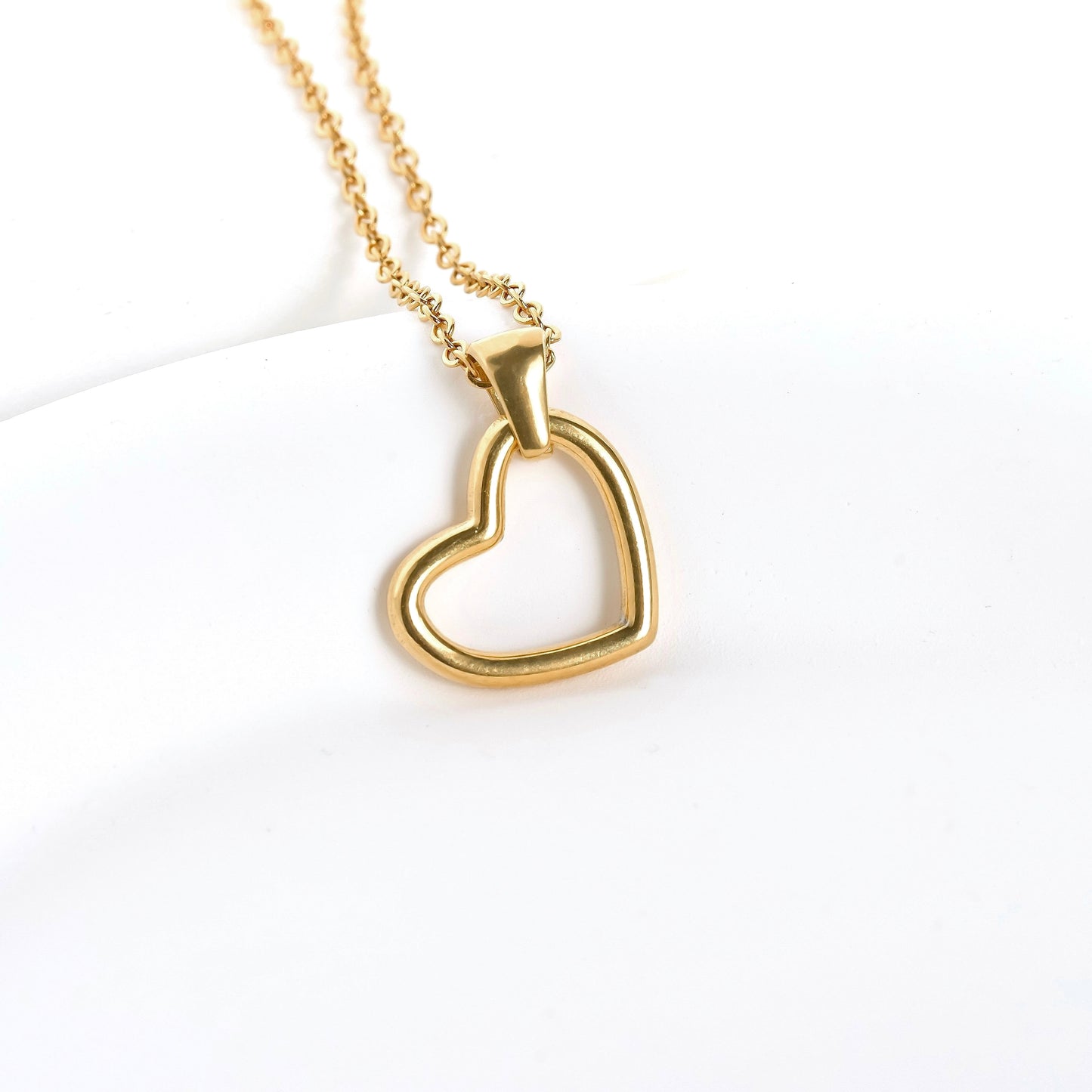 Gold cut-out heart pendant hanging sideways from a thin cable chain on a white background