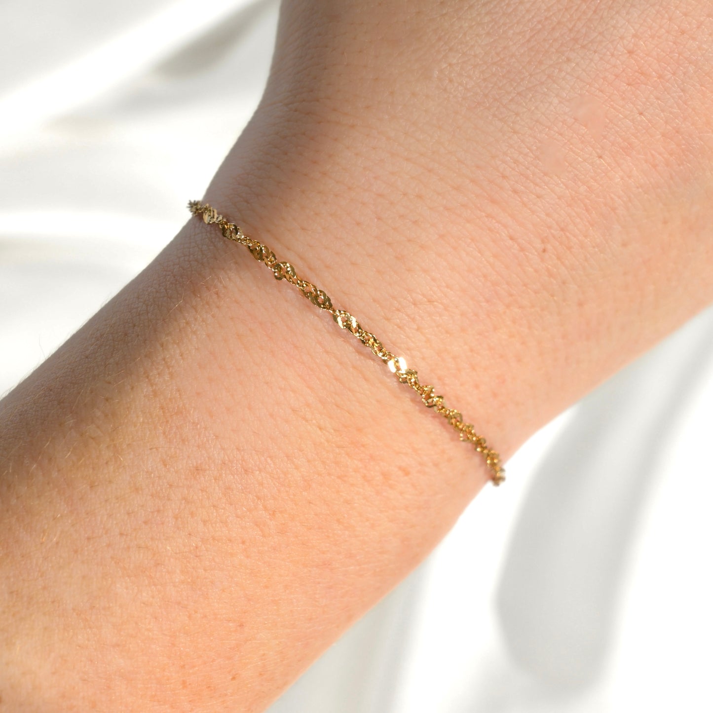 Gold twist chain bracelet on a wrist against a white background