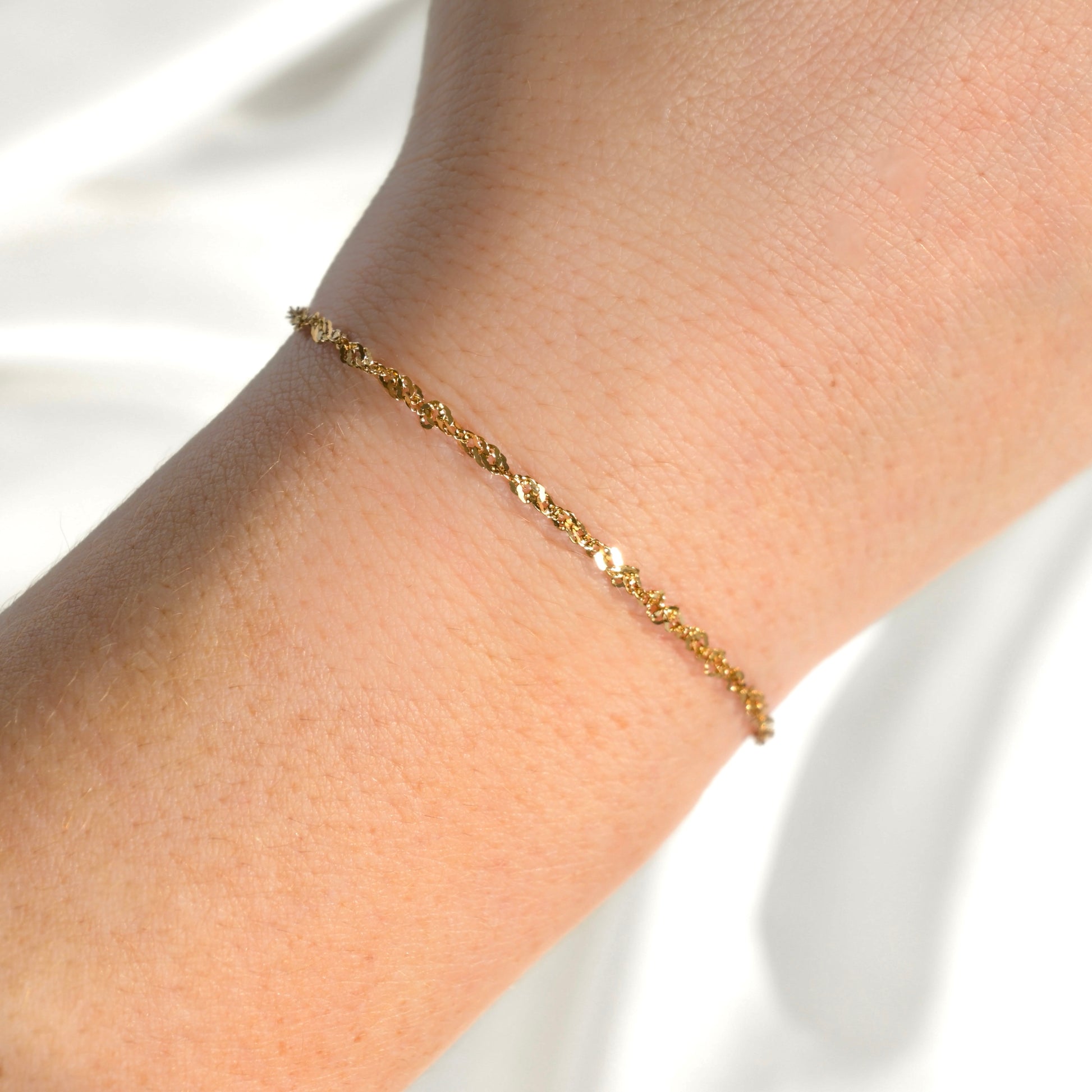 Gold twist chain bracelet on a wrist against a white background