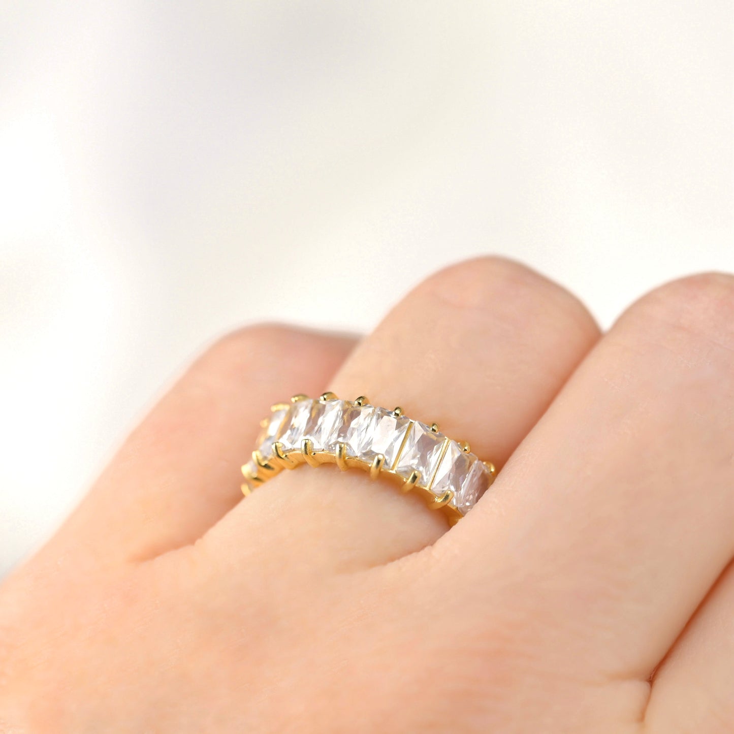 Gold ring with white baguette-cut gemstones on a hand against a light background