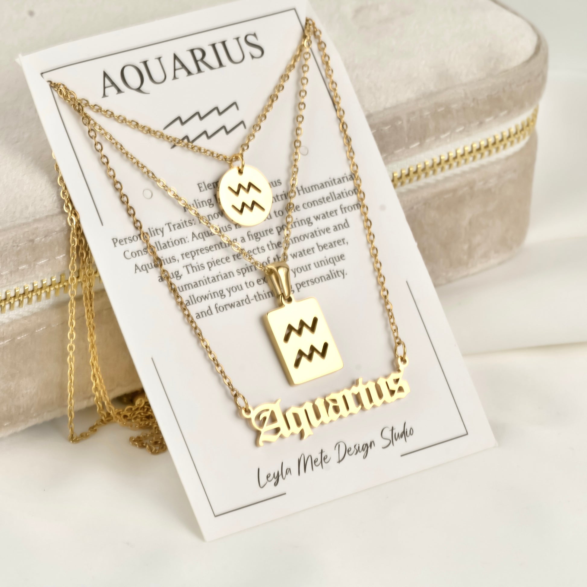 Gold Aquarius necklaces on a branded card with product details.