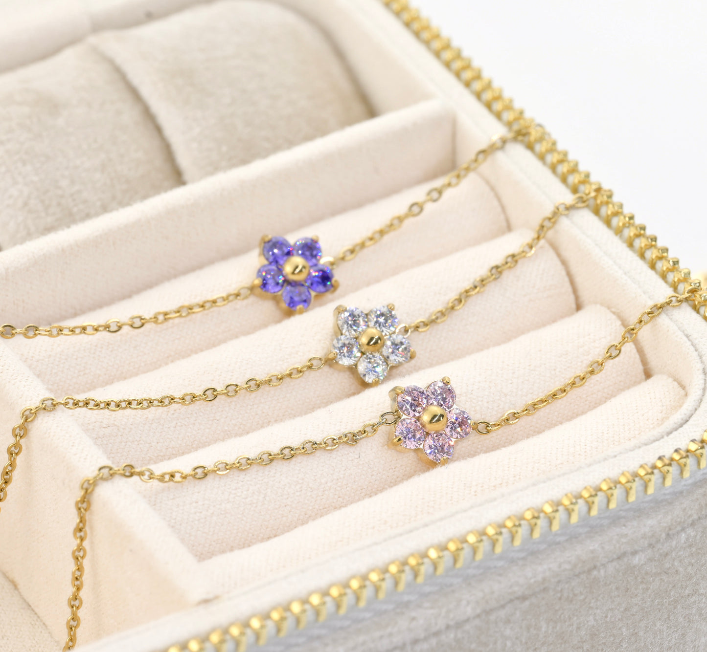 Gold bracelets with floral charms  featuring different colored stones on a beige jewelry box